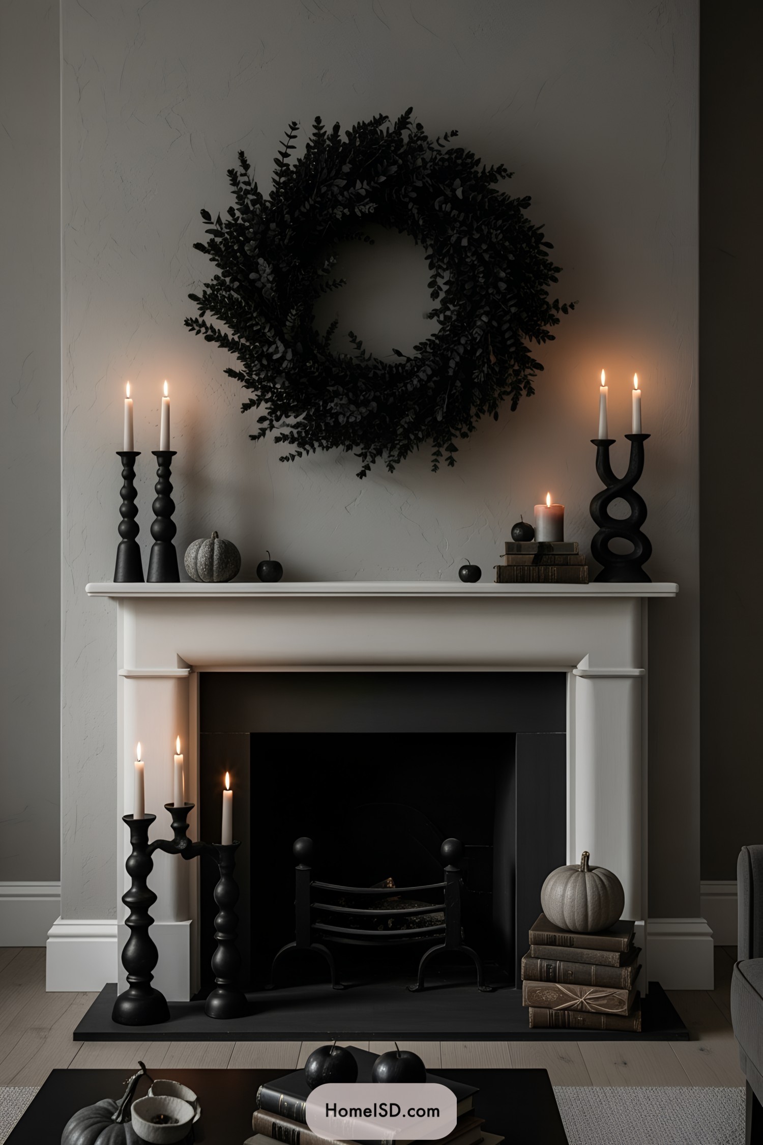 Dark wreath over a fireplace surrounded by black candlesticks and pumpkins