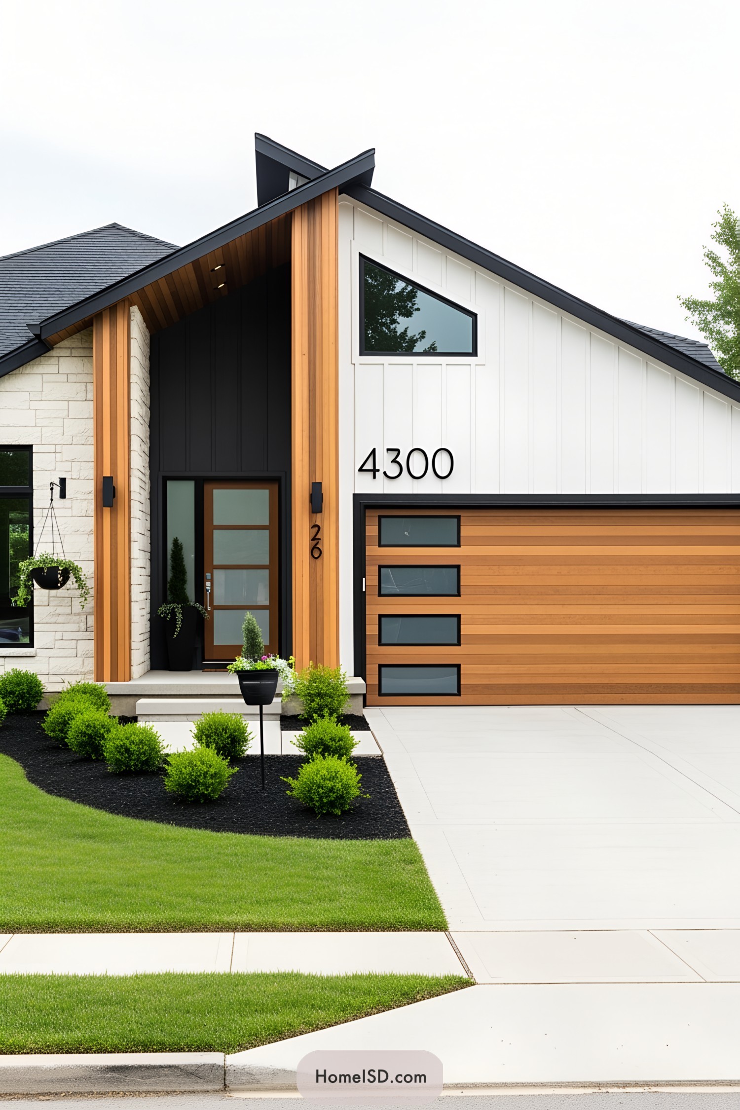Modern Curb Appeal with a streamlined entry area, exhibiting a contemporary aesthetic and minimalist design. The color scheme uses crisp white, charcoal gray, and warm natural wood accents. Architectural details include a prominent angled roofline and large street numbers above a new horizontally slatted wooden garage door. Exterior stonework remains on the front façade, paired with sleek black trim and bold vertical wood siding near the entrance. Concrete driveway and pathway are clean and simple. Furnishings are absent, but minimalist landscaping features manicured lawn, dark mulch beds, neatly trimmed shrubs, and a suspended planter, enhancing the modern style.