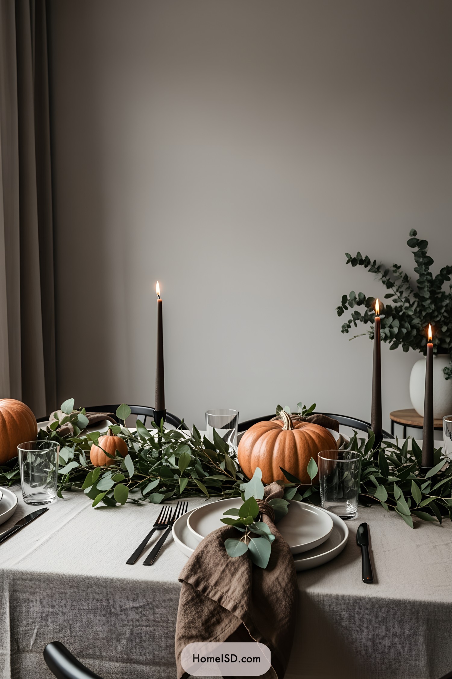 Thanksgiving table adorned with pumpkins, greenery, and tall candles