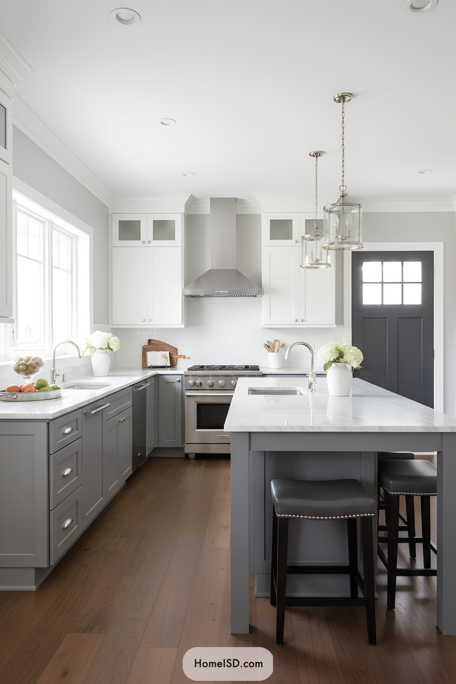 Light gray shaker cabinets, white uppers, marble-look counters, pendant lights, stainless range, and warm wood floors
