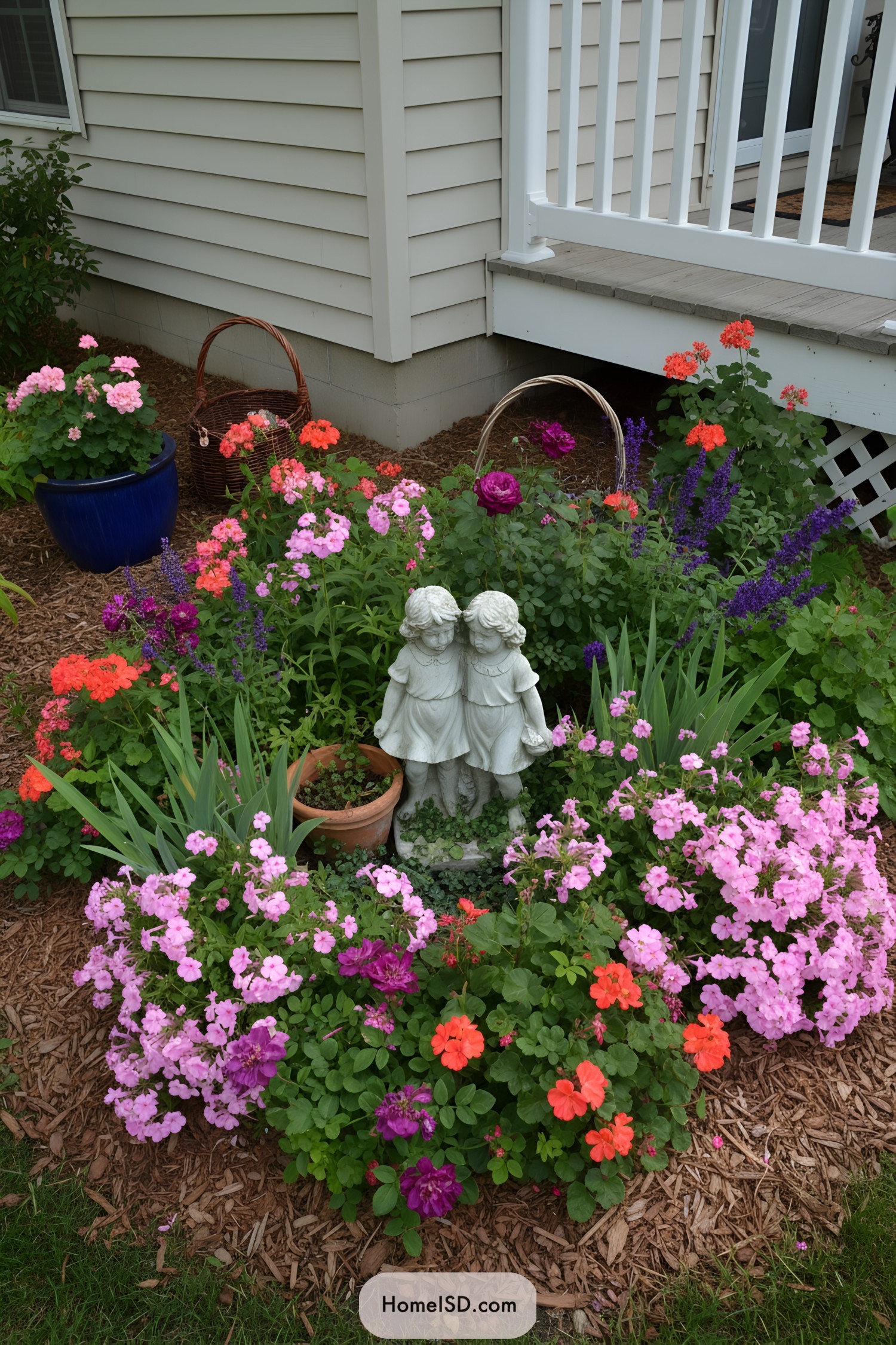 Small garden with twin-girl statue surrounded by pink, purple, and orange flowers near a porch