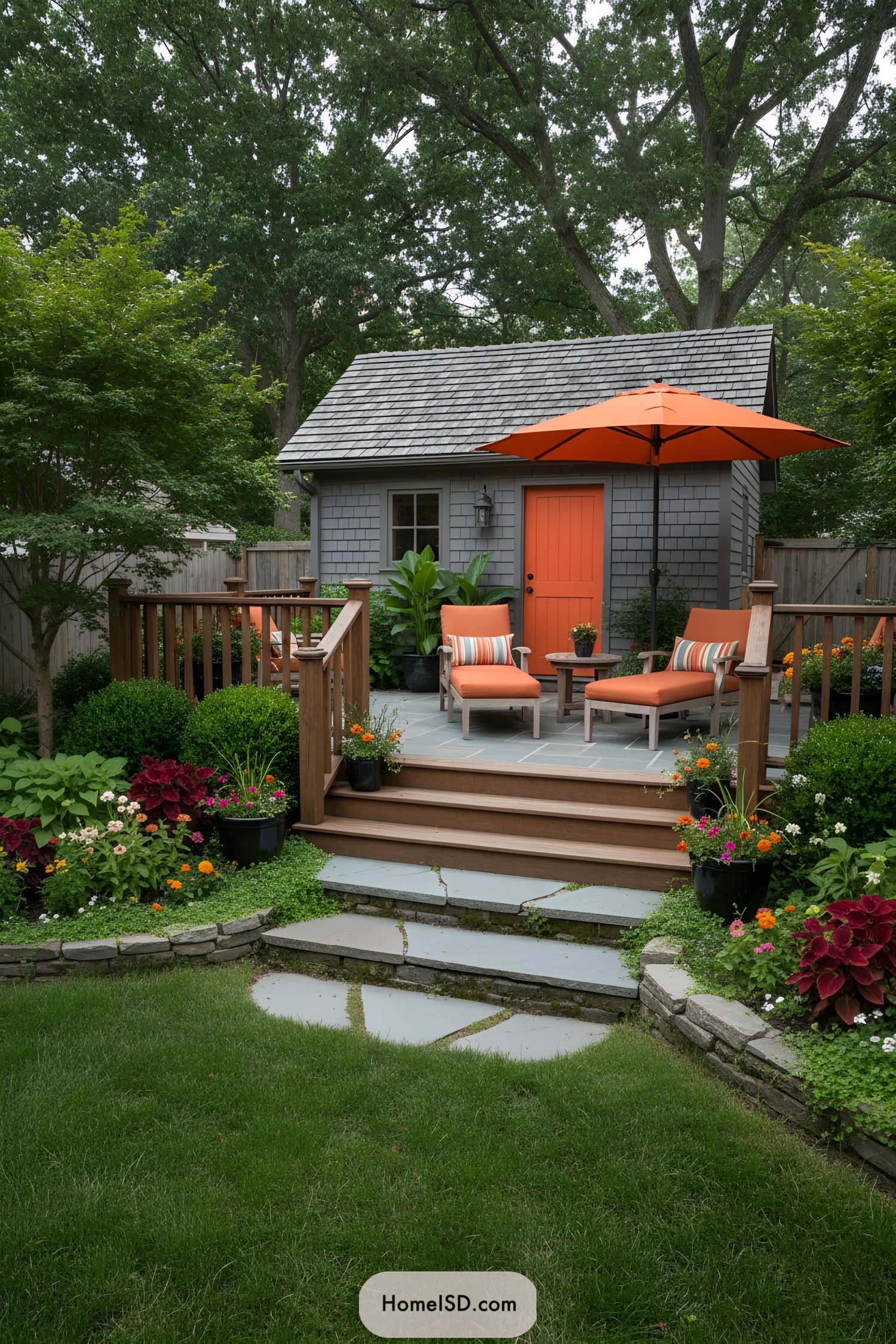 Small patio with gray shed, orange door, and lounge chairs under an orange umbrella; surrounded by lush plantings and stone steps