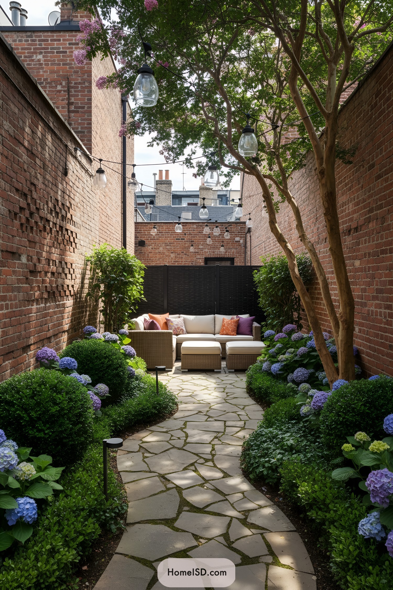 Cozy brick-walled courtyard with stone path, string lights, and hydrangea borders leading to a rattan lounge