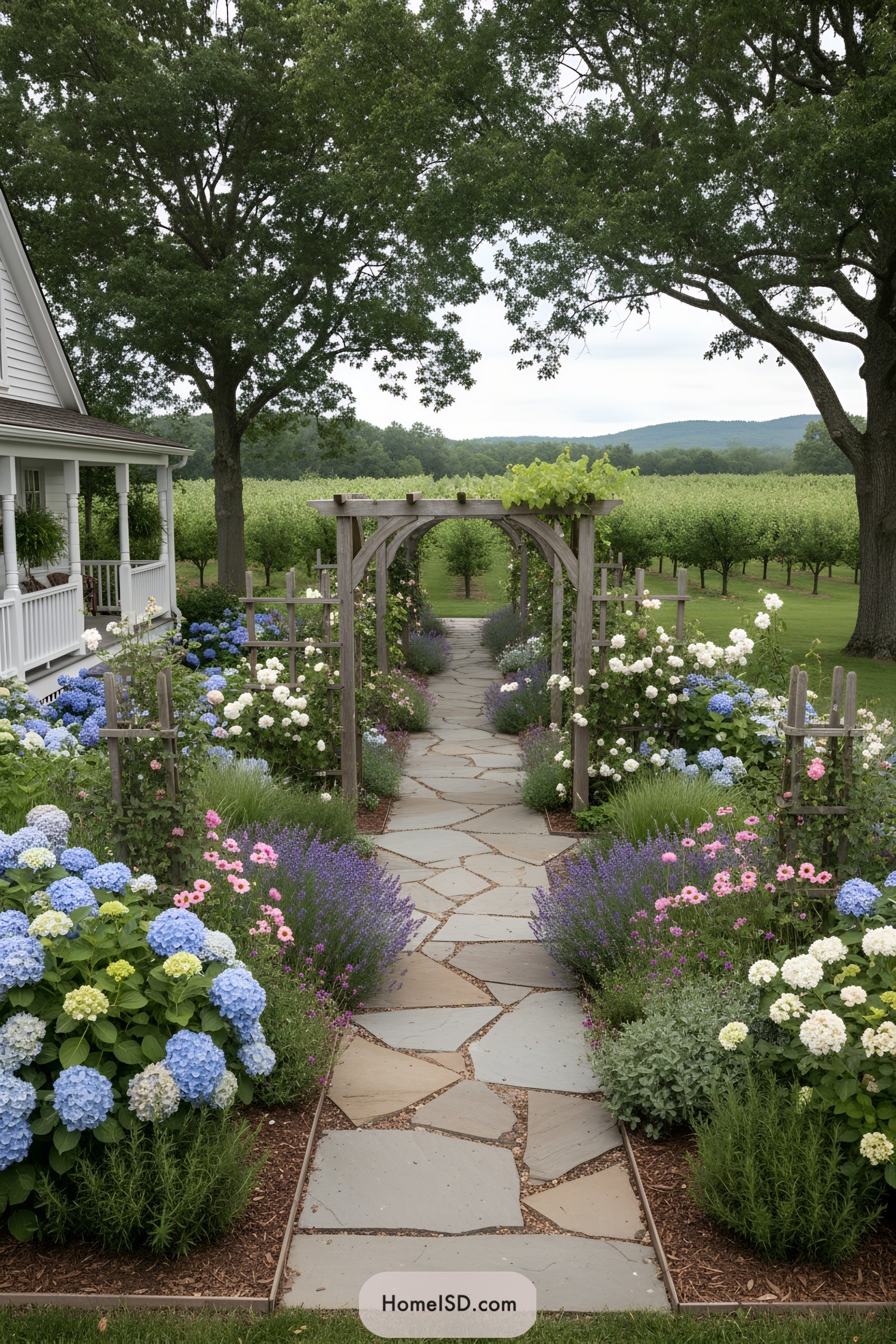 Flagstone garden path under wooden arbors bordered by colorful flowering beds leading to an orchard