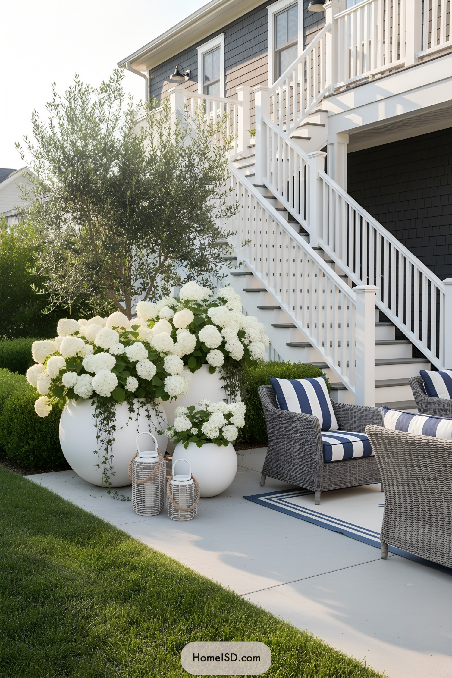 Coastal-style patio with white hydrangeas, round planters, and striped lounge seating