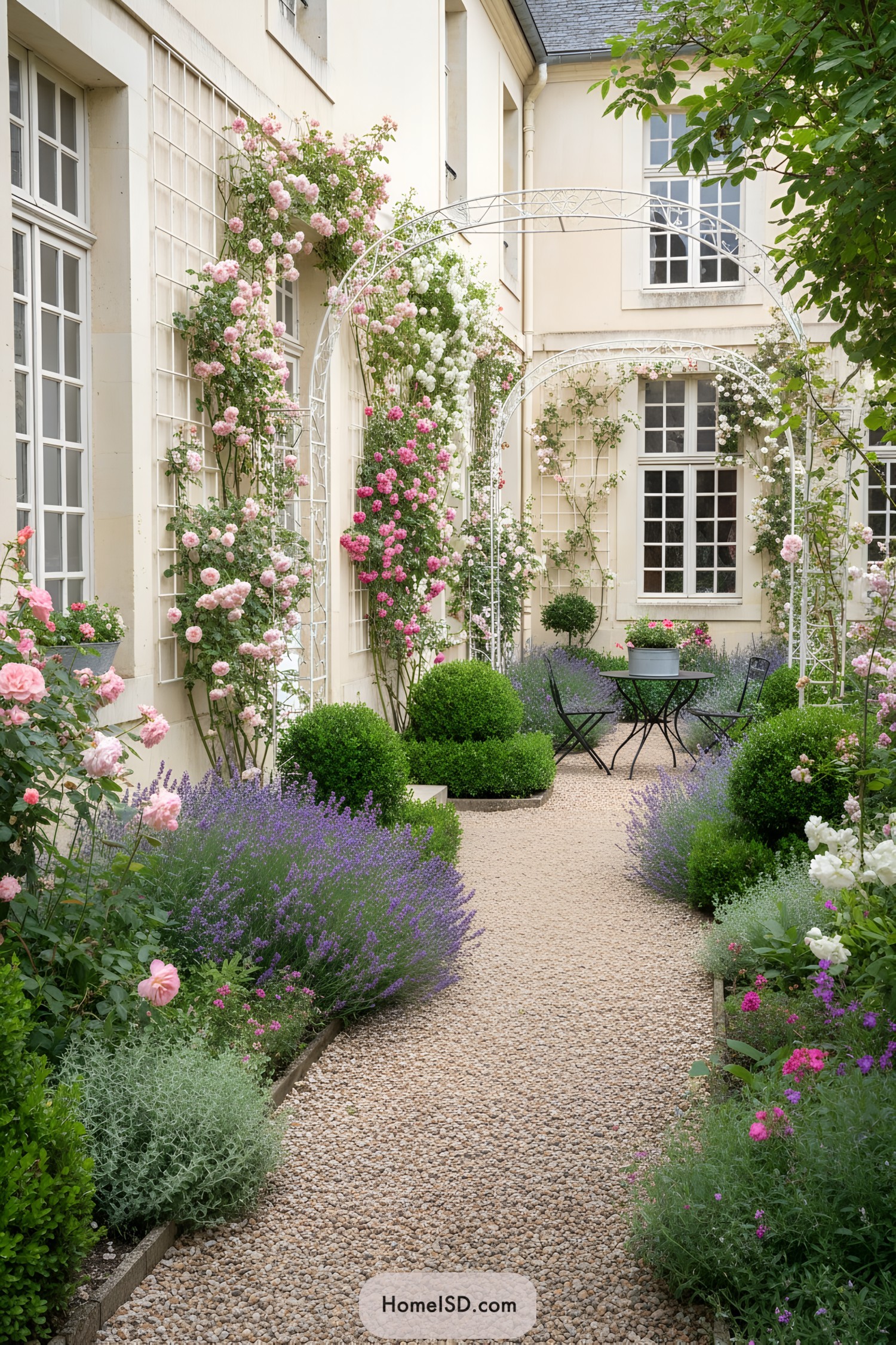 Narrow French courtyard with gravel path, roses, lavender, and bistro set
