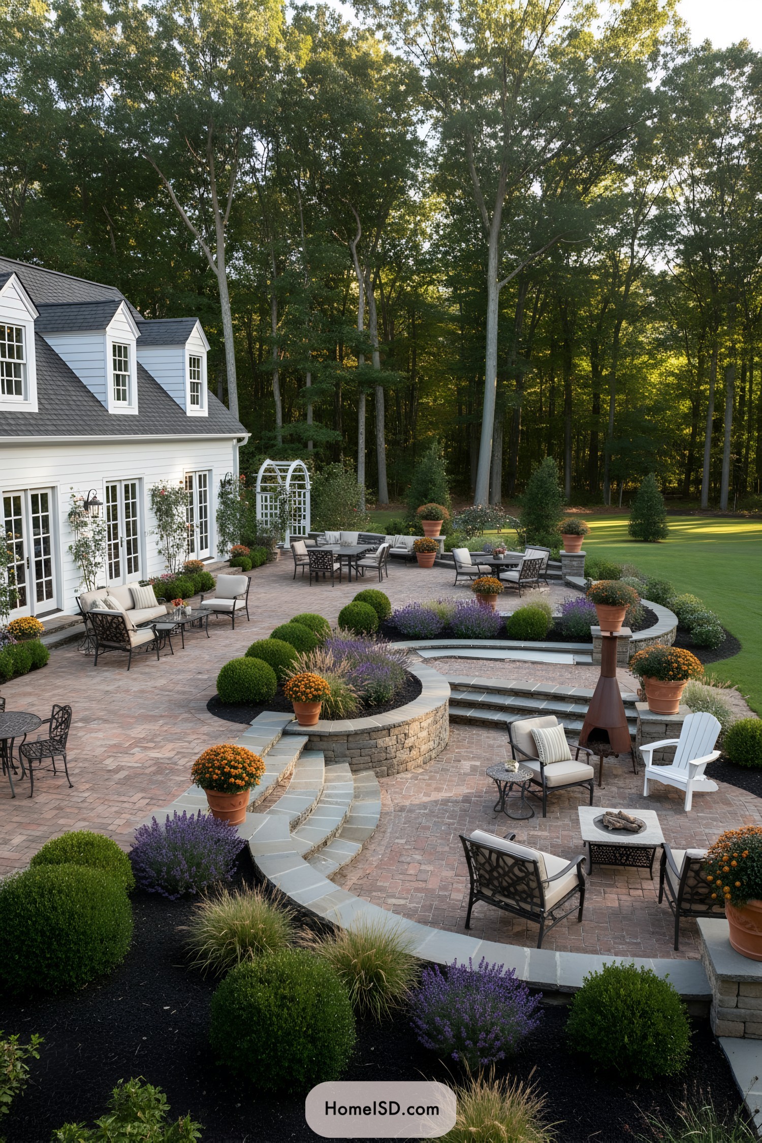Multi level brick patio with layered seating areas, potted plants, and curved stone walls beside a forested backyard