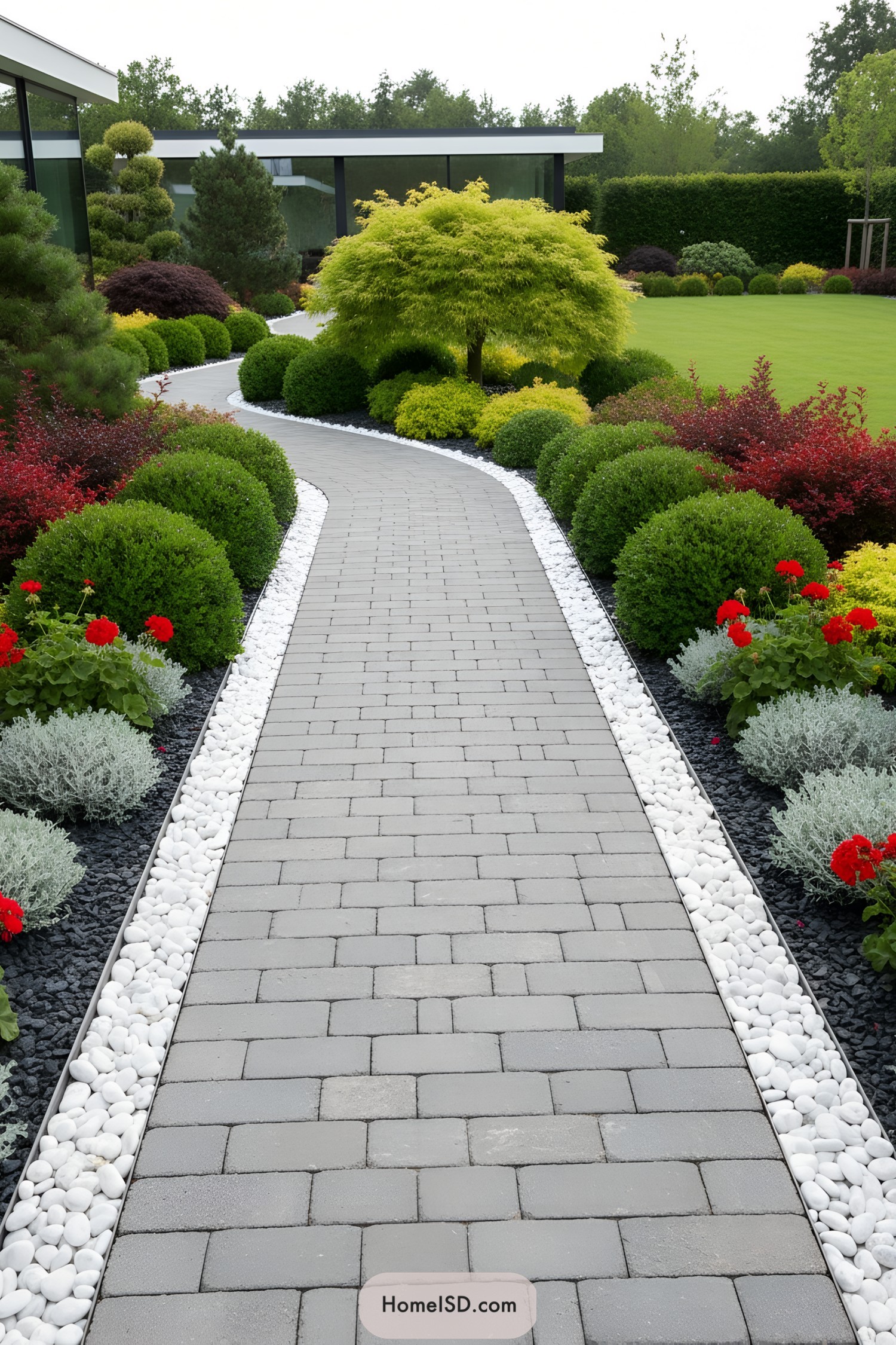 Curved gray paver path bordered by white stones and manicured shrubs in a modern garden