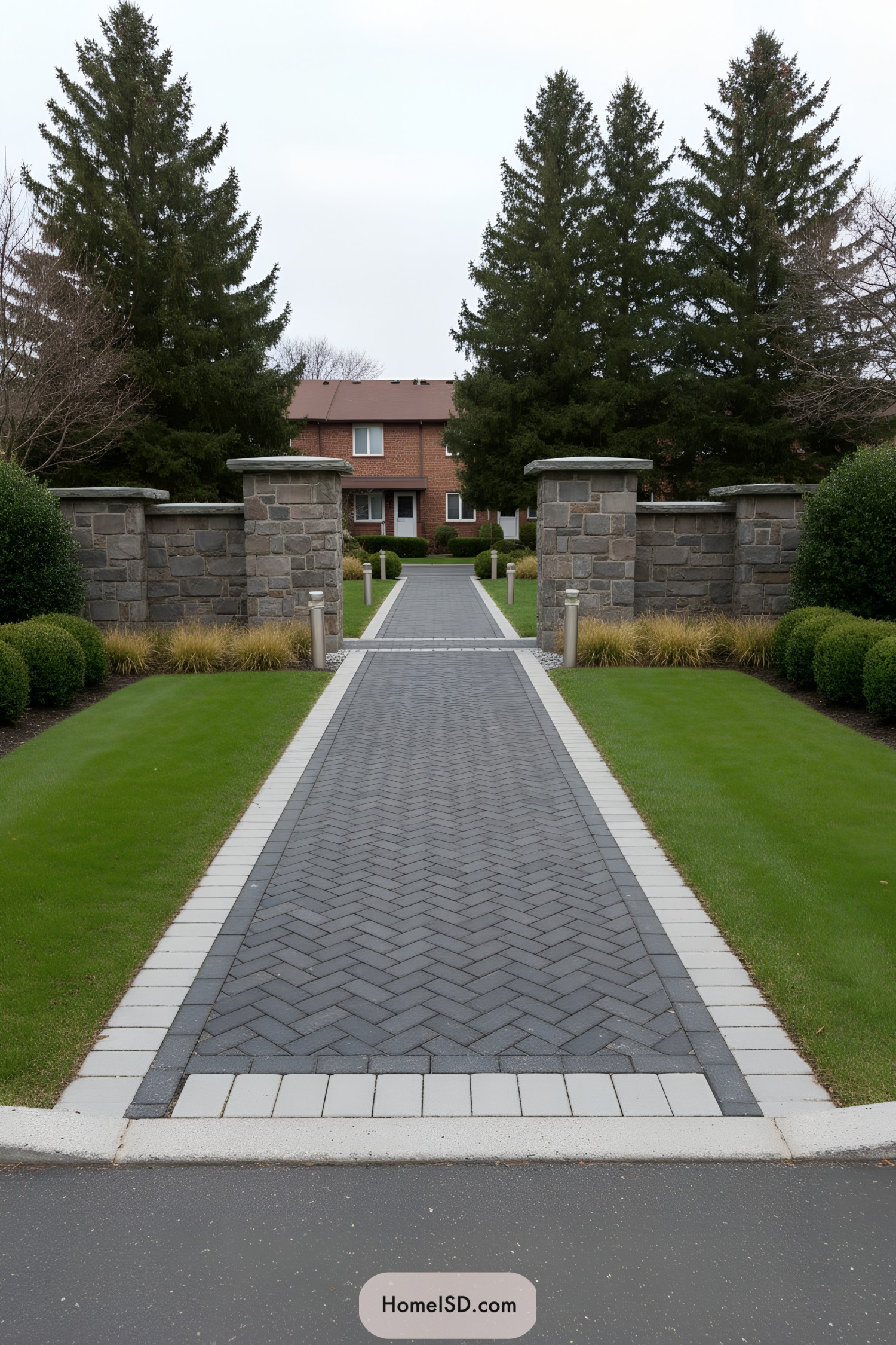 Long herringbone paver path framed by manicured lawns and stone entry pillars