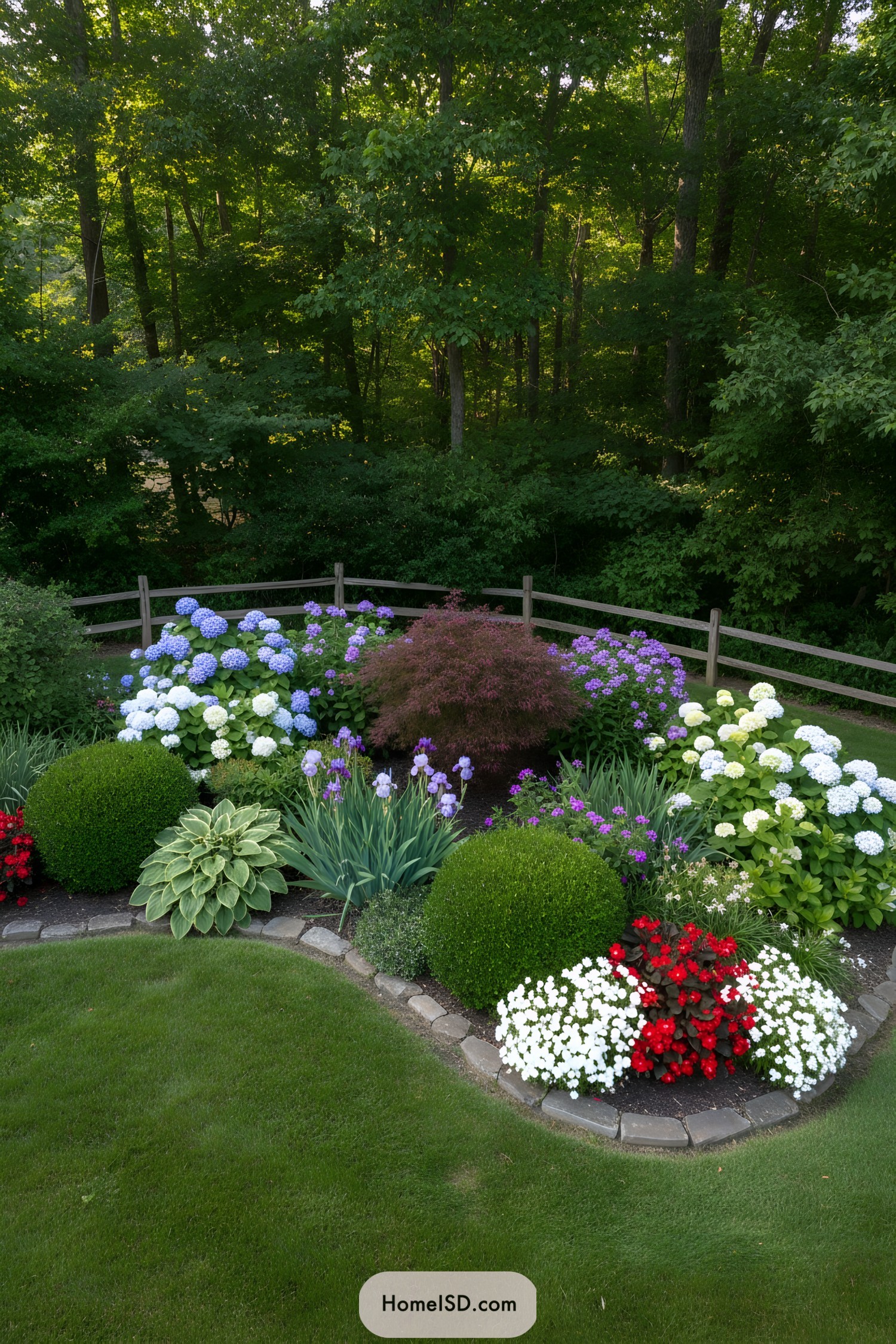 Curved flower bed with colorful blooms along a split-rail fence by a wooded backdrop
