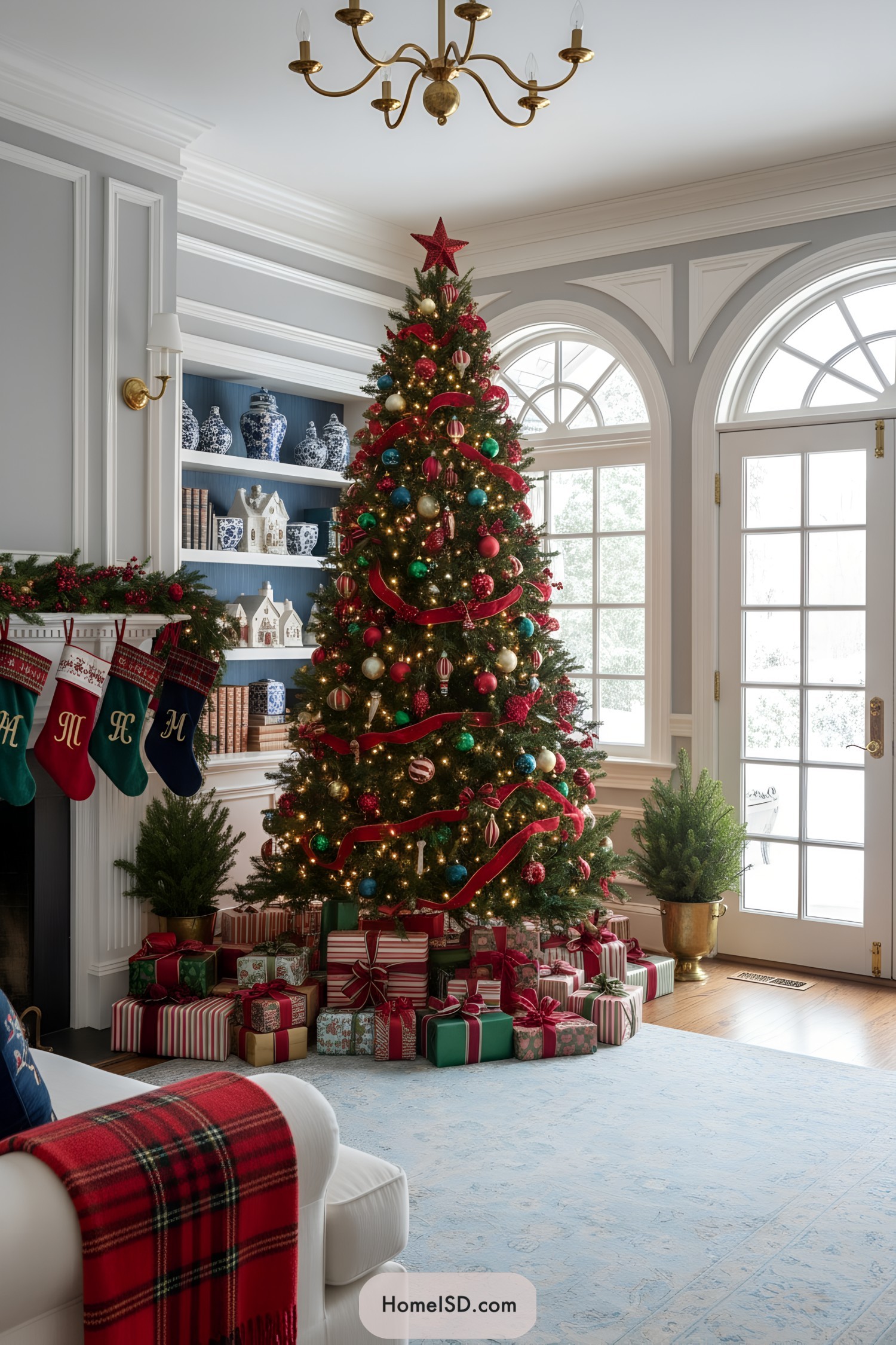 Traditional tree with red ribbons, multicolor ornaments, and warm lights beside French doors, surrounded by wrapped gifts