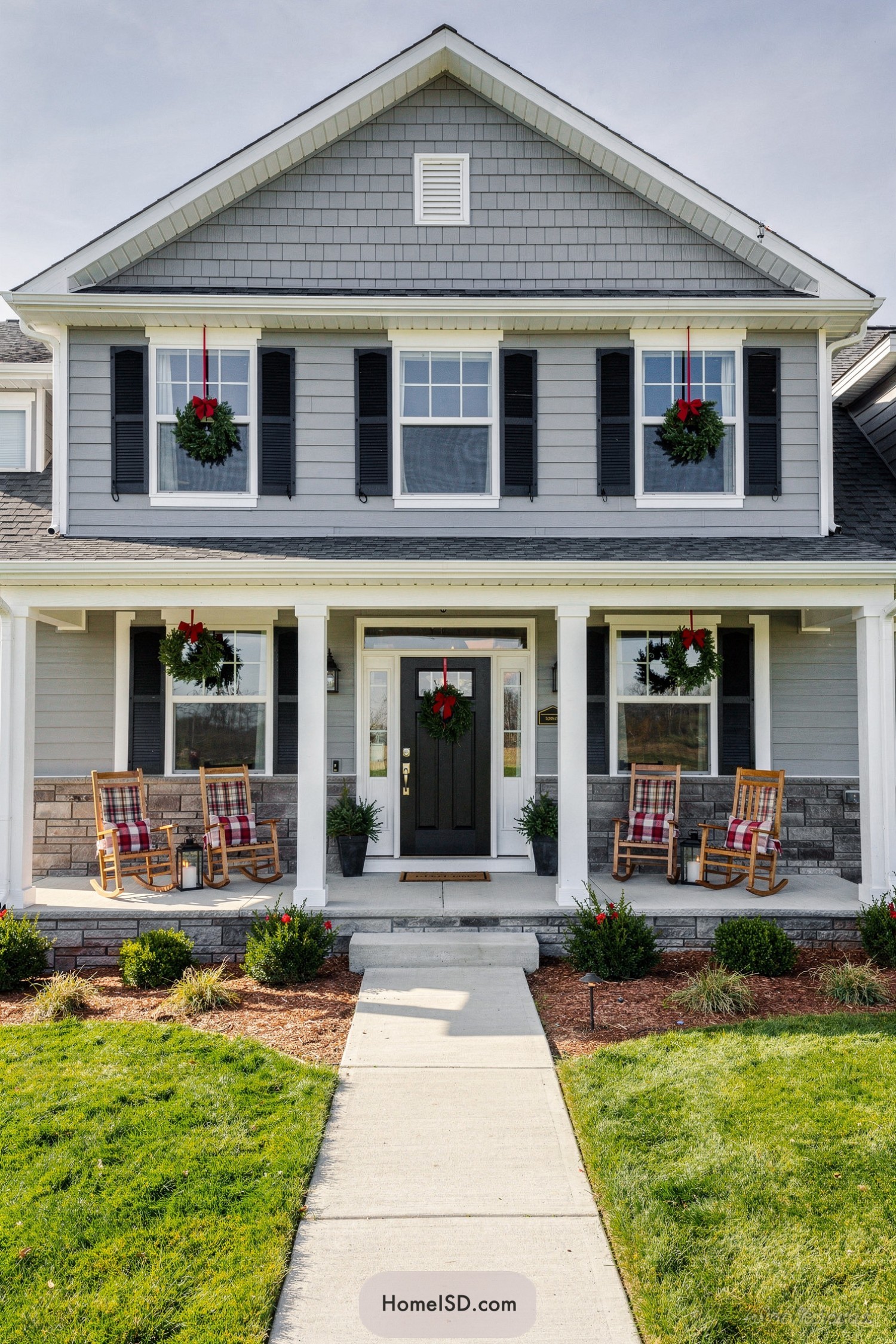 Gray suburban house with matching red-bow wreaths on windows and door, flanked by rocking chairs on the front porch