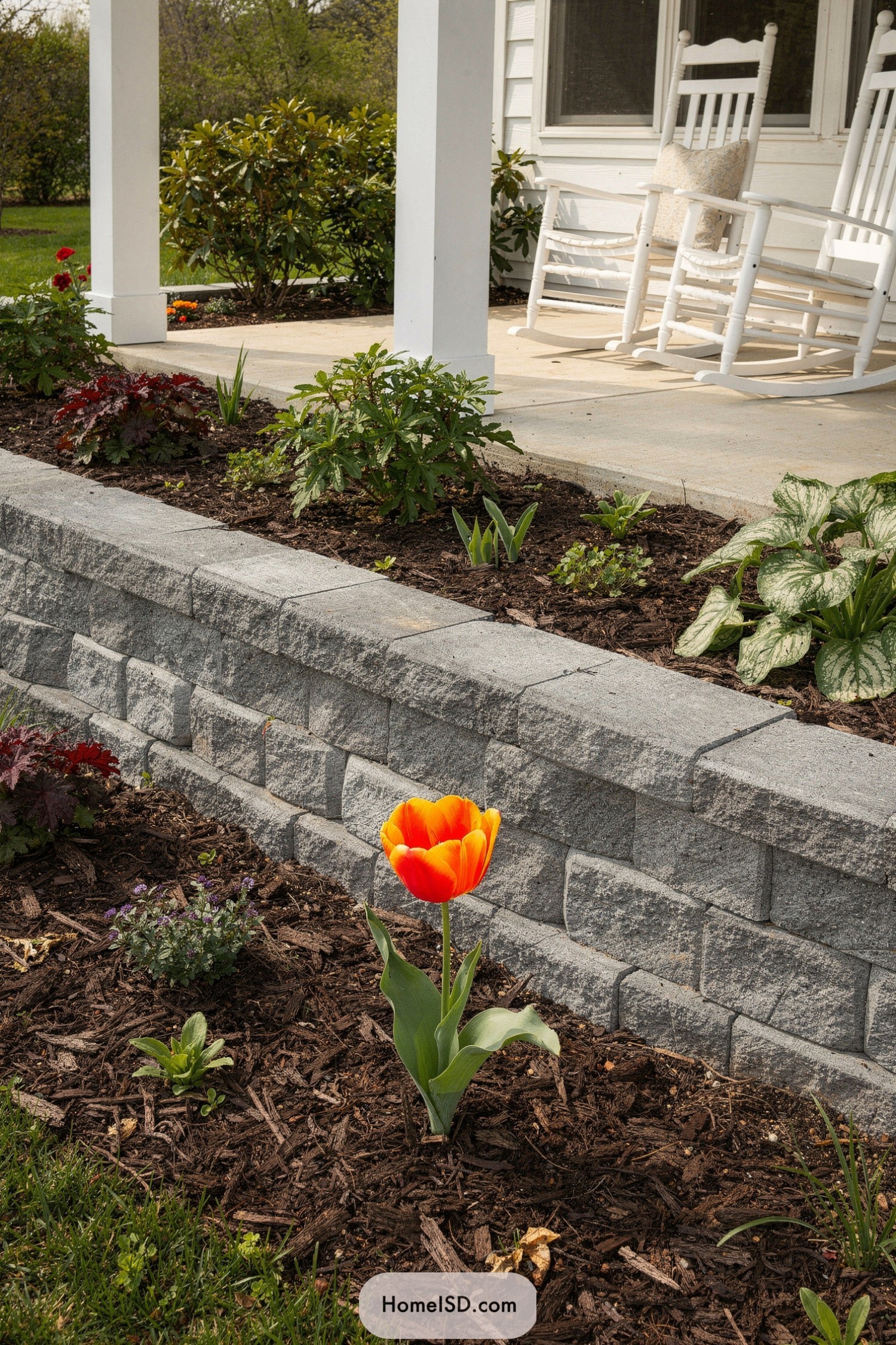 Raised stone flower bed with bright tulip and porch rockers in background