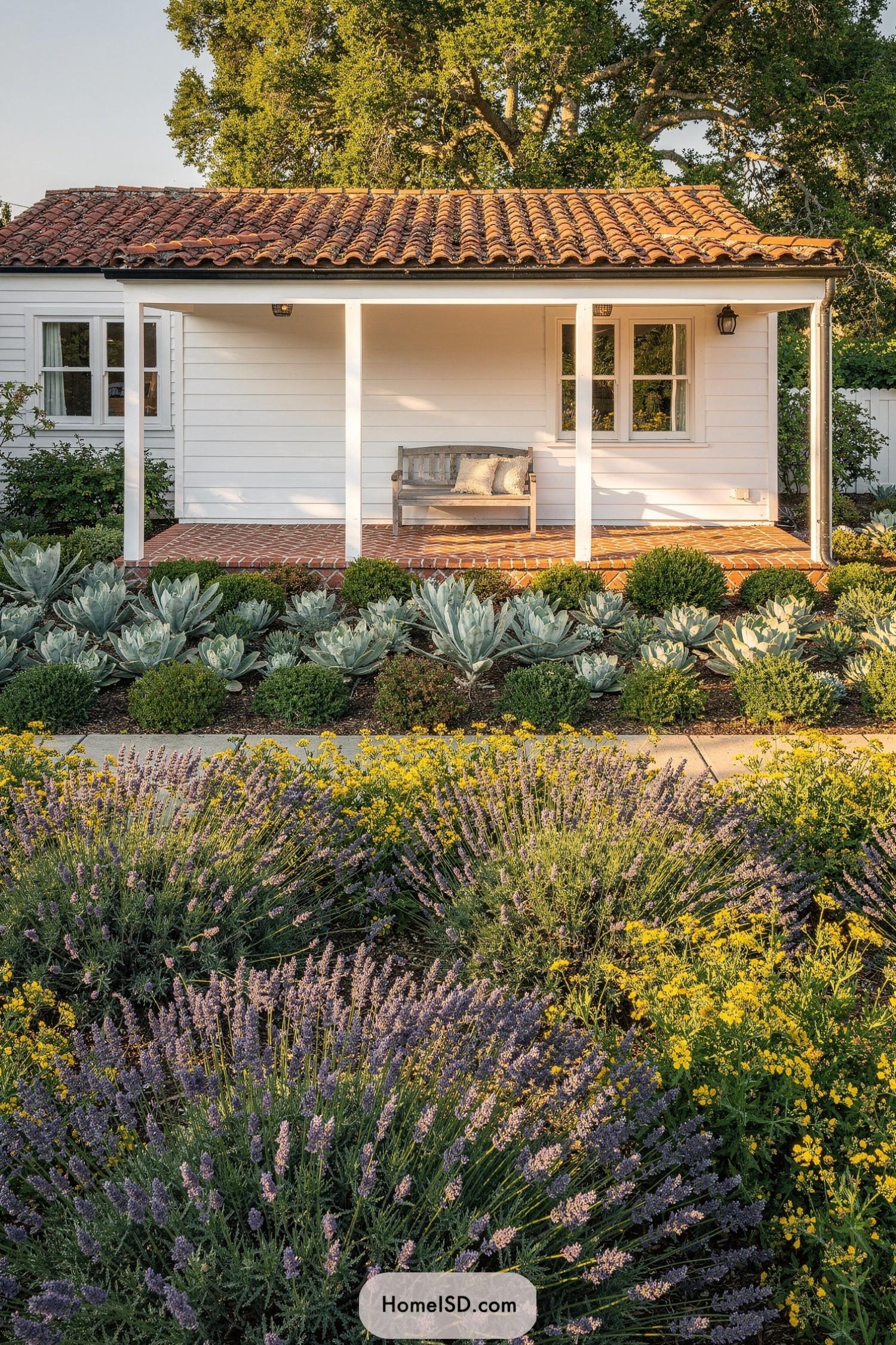 Cozy white cottage porch with terracotta roof framed by lavender, yellow flowers, and sculptural succulents