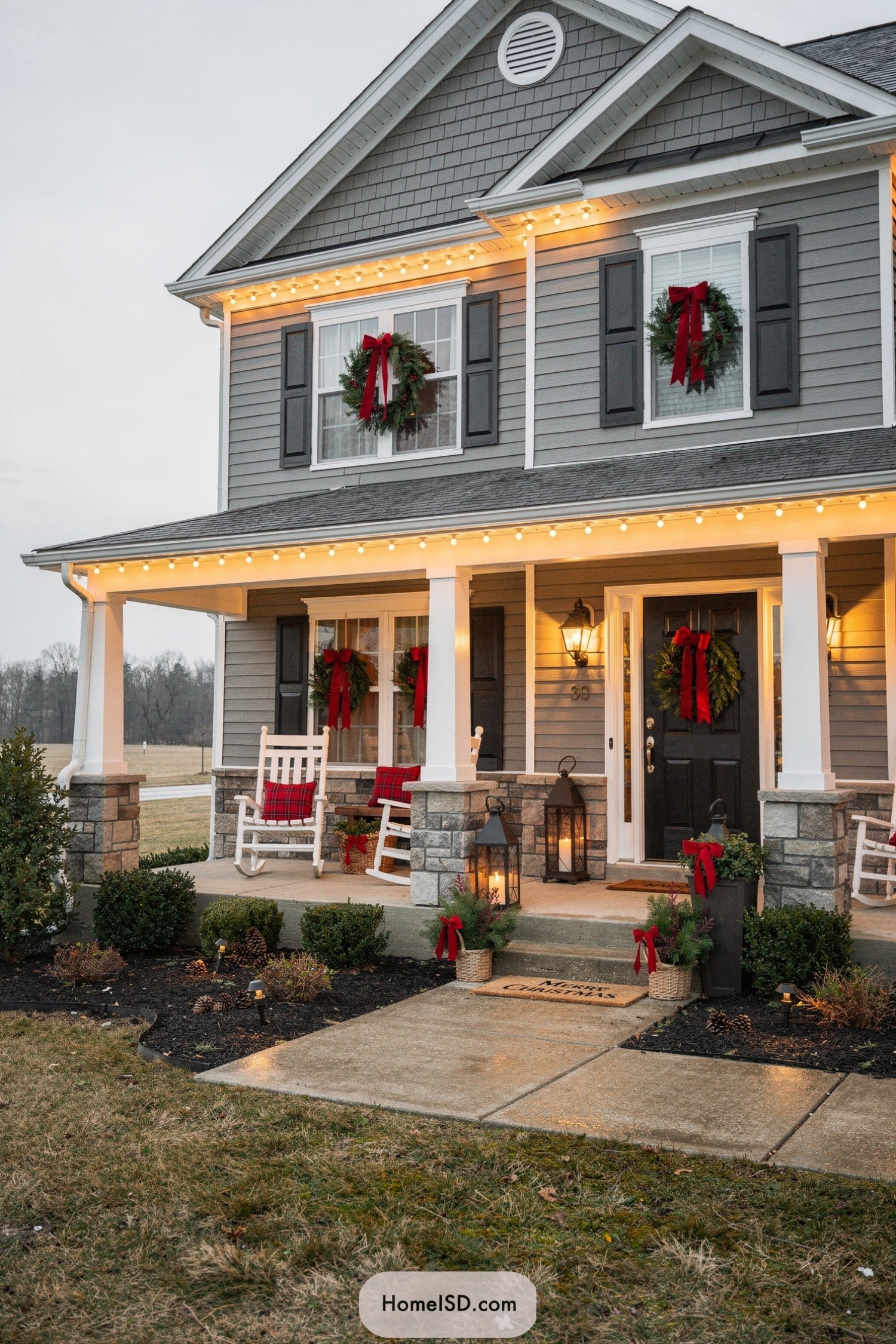 Gray house with red-bowed Christmas window wreaths and warm porch decor
