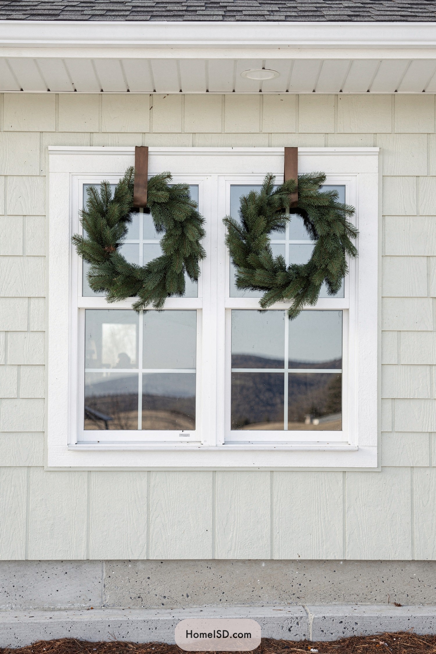 Two simple evergreen wreaths hanging on a double exterior window