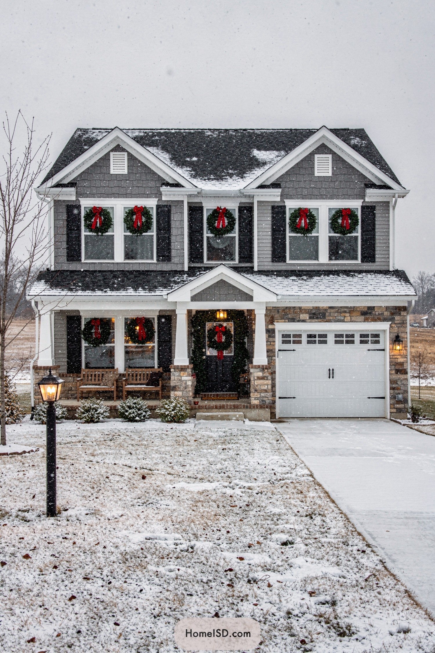 Gray two story house with red-bowed wreaths on each window during a light snowfall