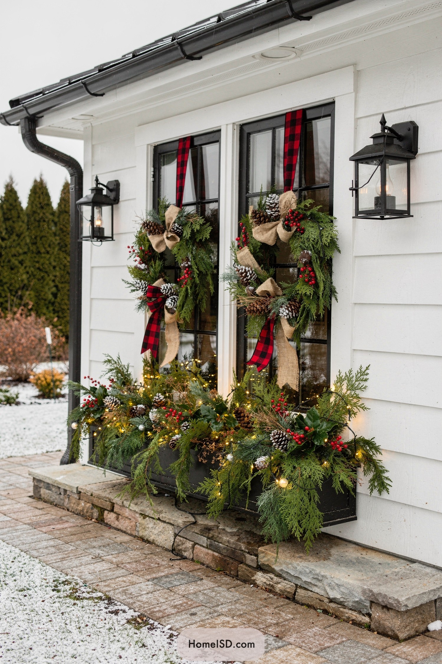 Double black-framed windows with plaid-ribbon wreaths and evergreen window boxes