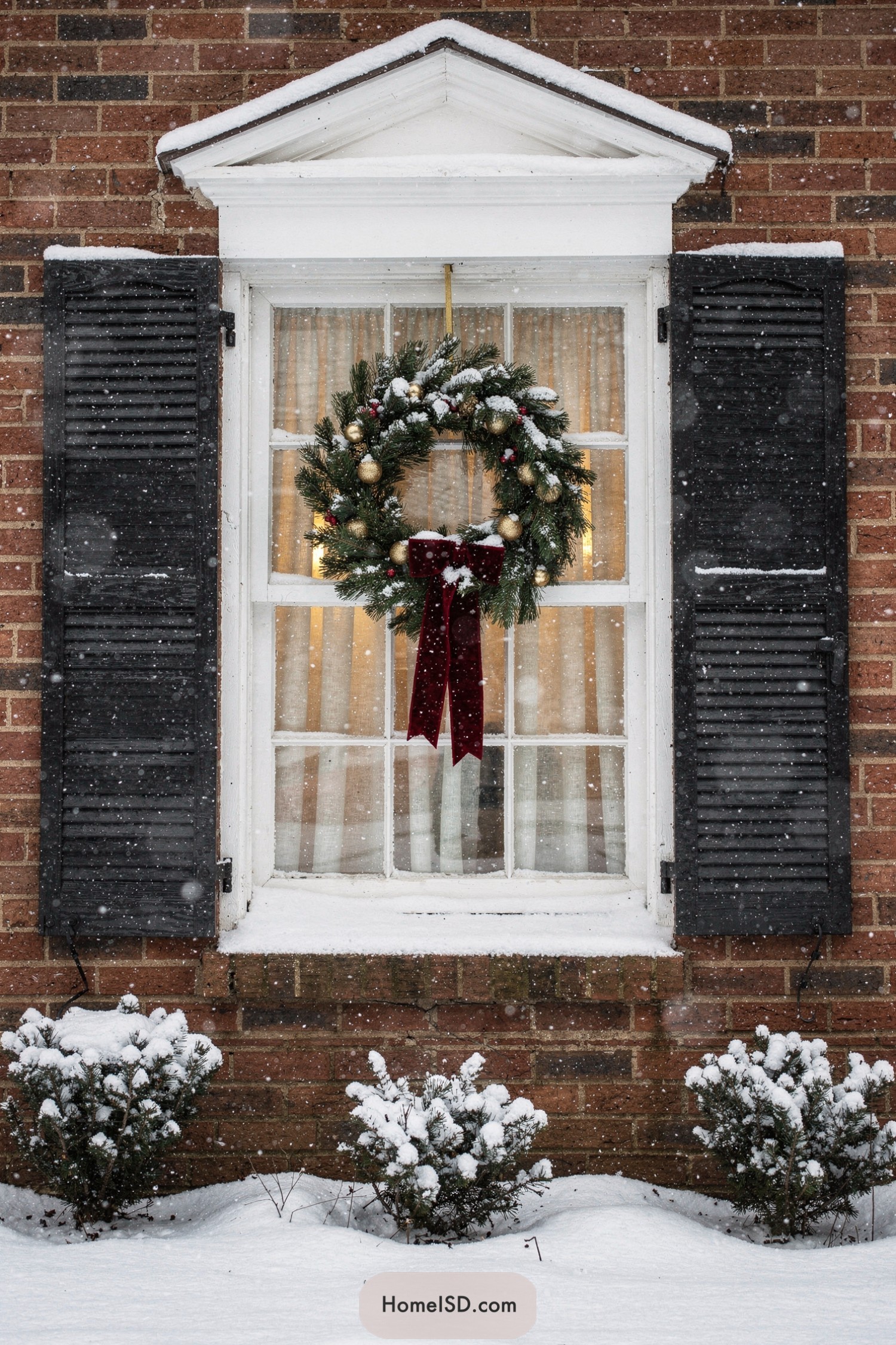 Snowy brick house window with lit wreath