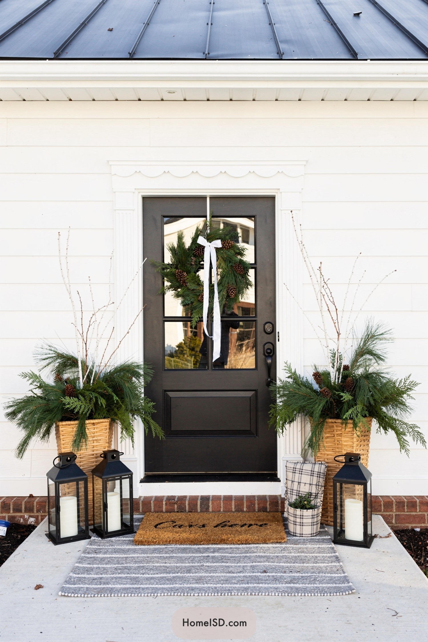Black front door with winter greenery planters and lanterns