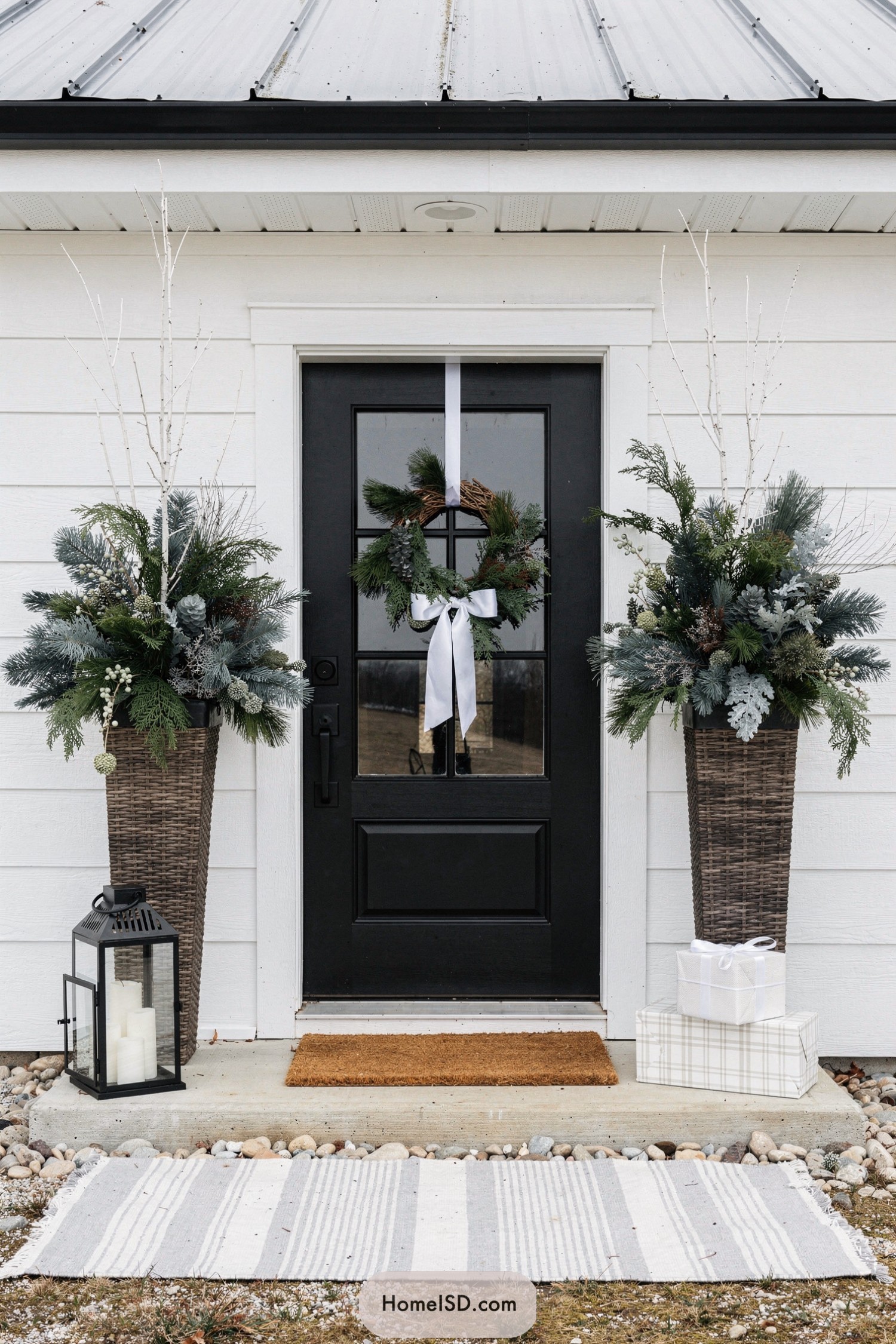 Black door with winter wreath and tall evergreen porch planters