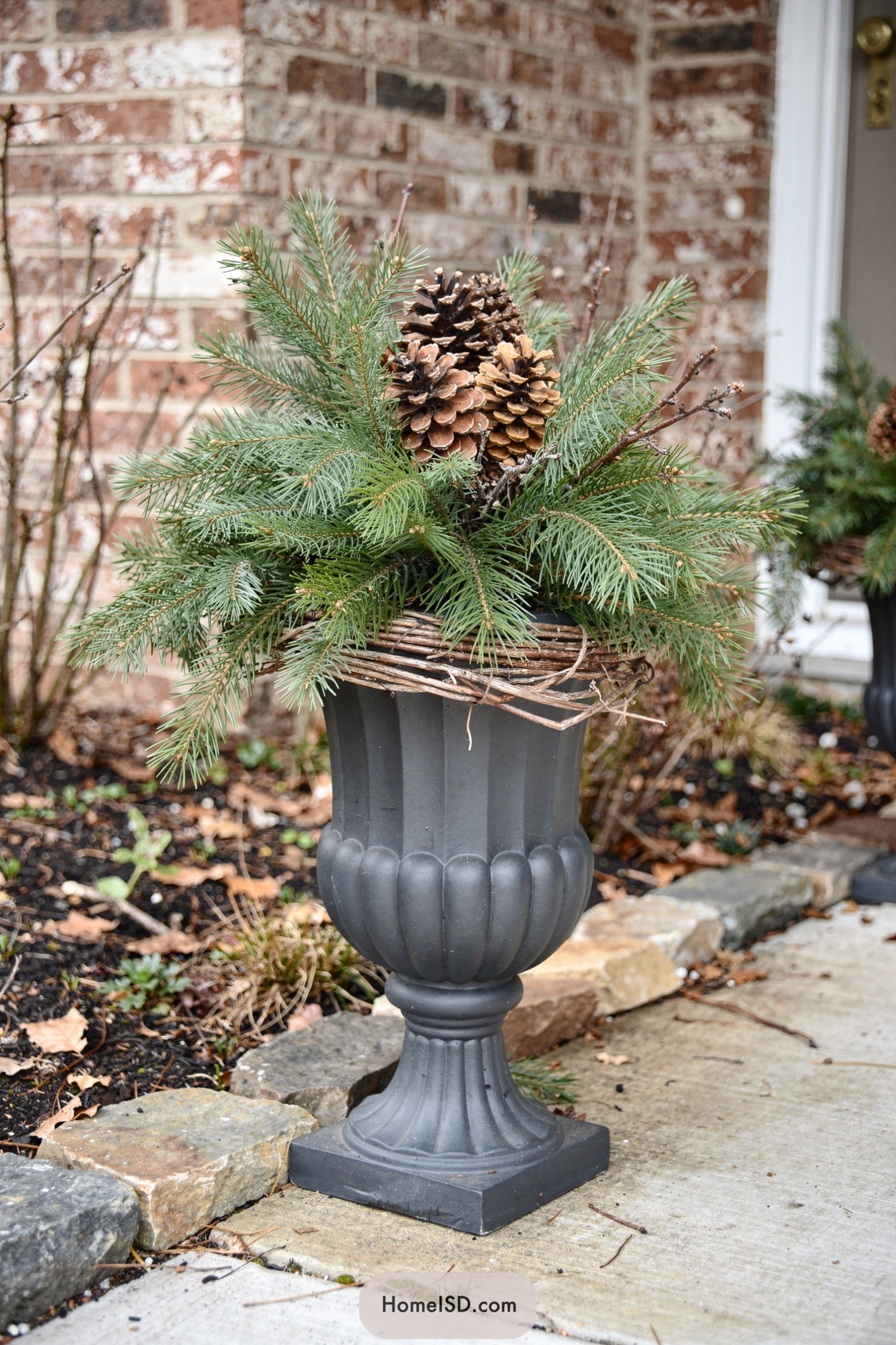 Tall gray urn planter with evergreen branches and pinecones on a winter porch