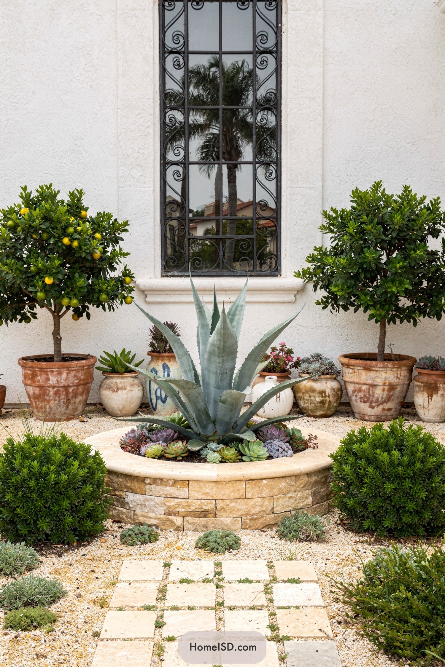 Mediterranean courtyard with central agave planter, potted citrus trees, and gravel path