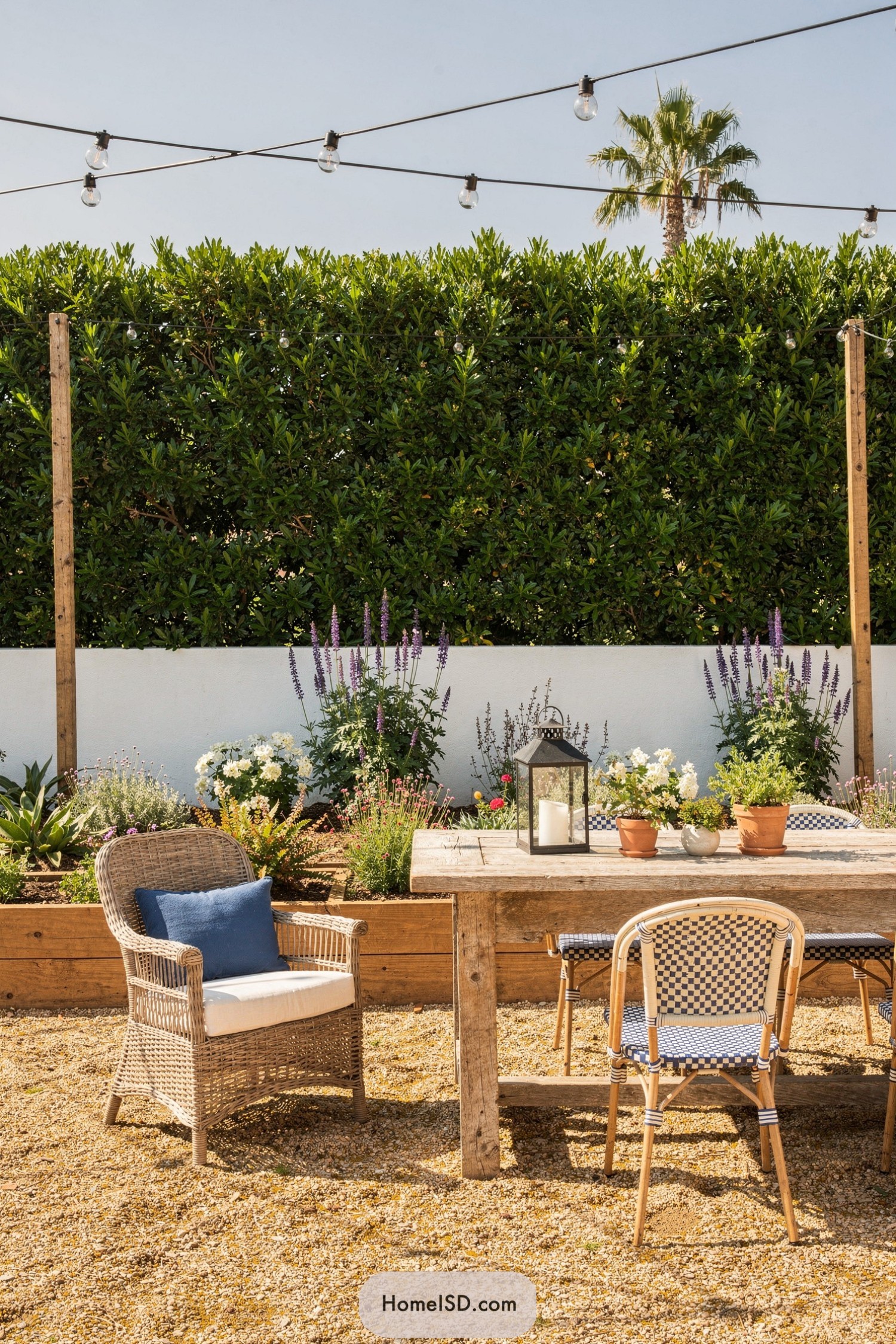 Outdoor dining nook framed by a tall privacy hedge and blooming border