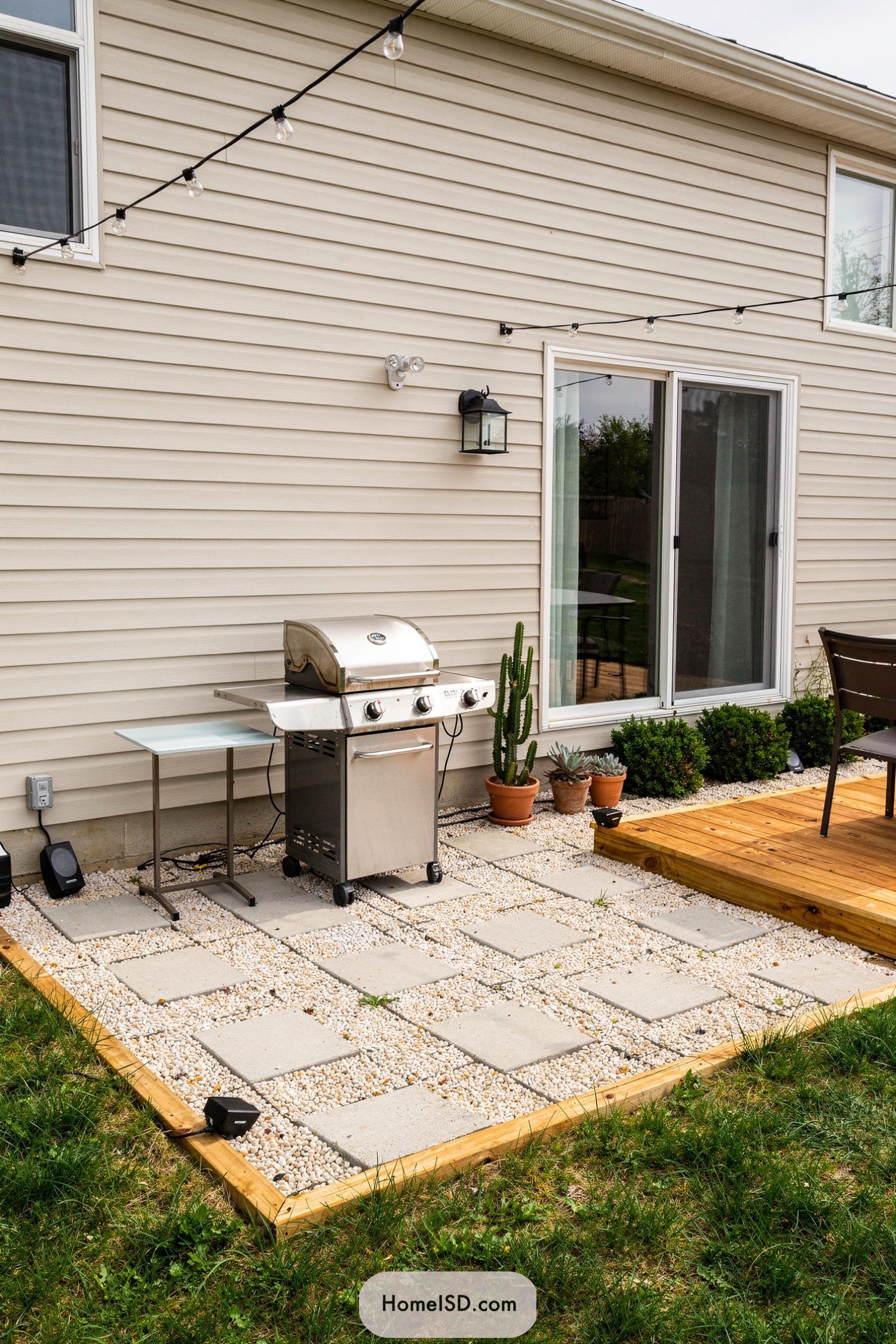 Small backyard grill area on a paver and pebble patio beside a wooden deck