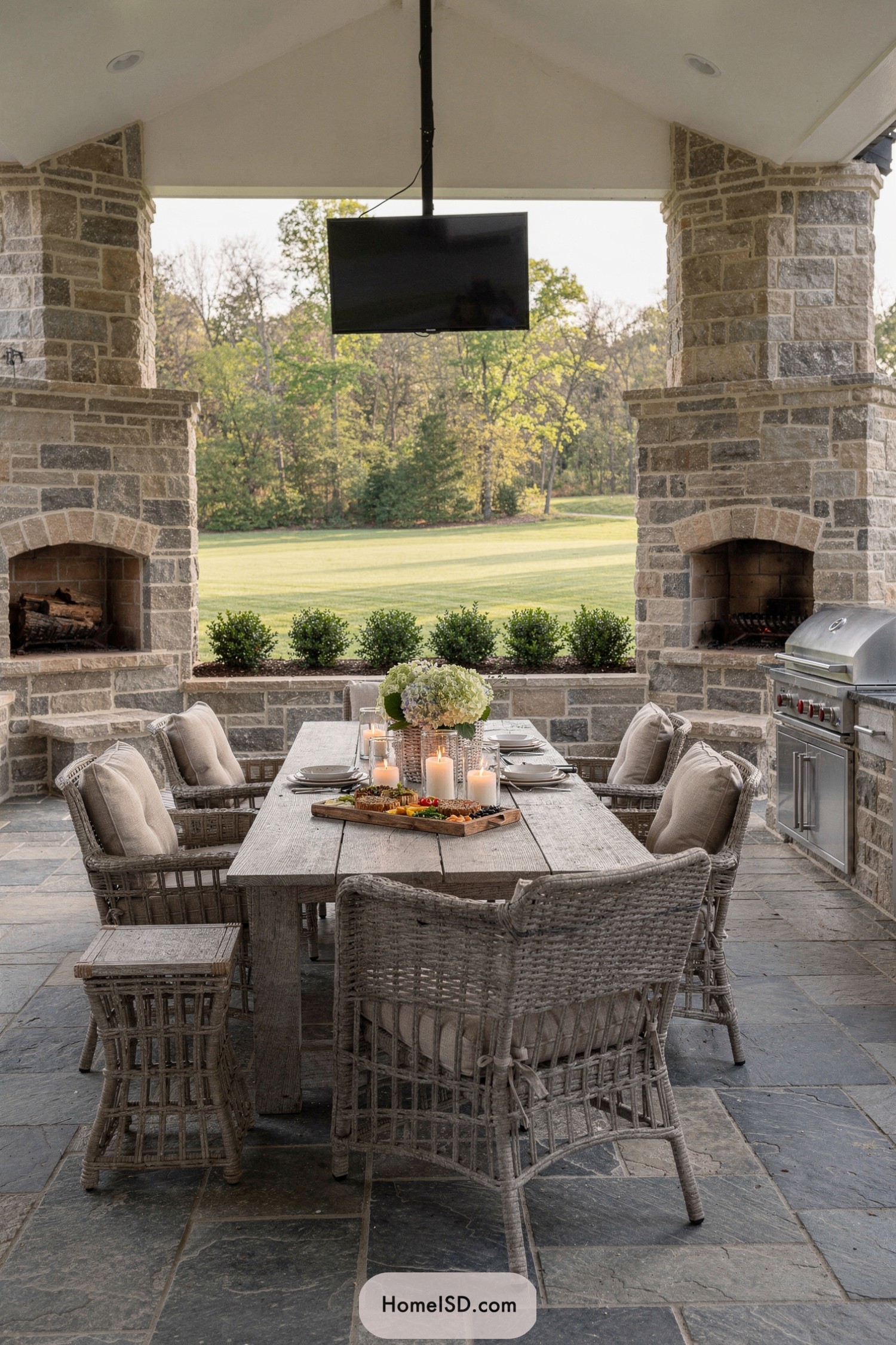 Covered stone patio with grill and rustic dining set overlooking a lawn