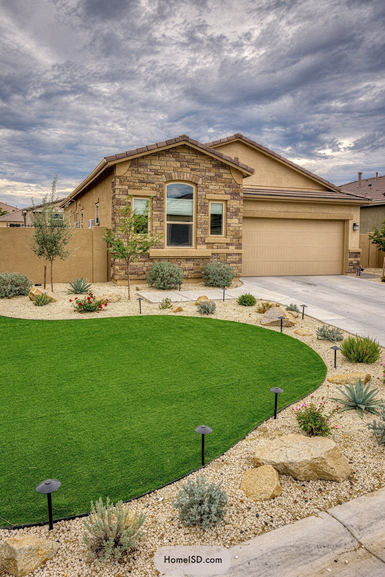 Suburban desert home with a sweeping curved artificial turf lawn edged by light gravel, boulders, and drought-tolerant plants