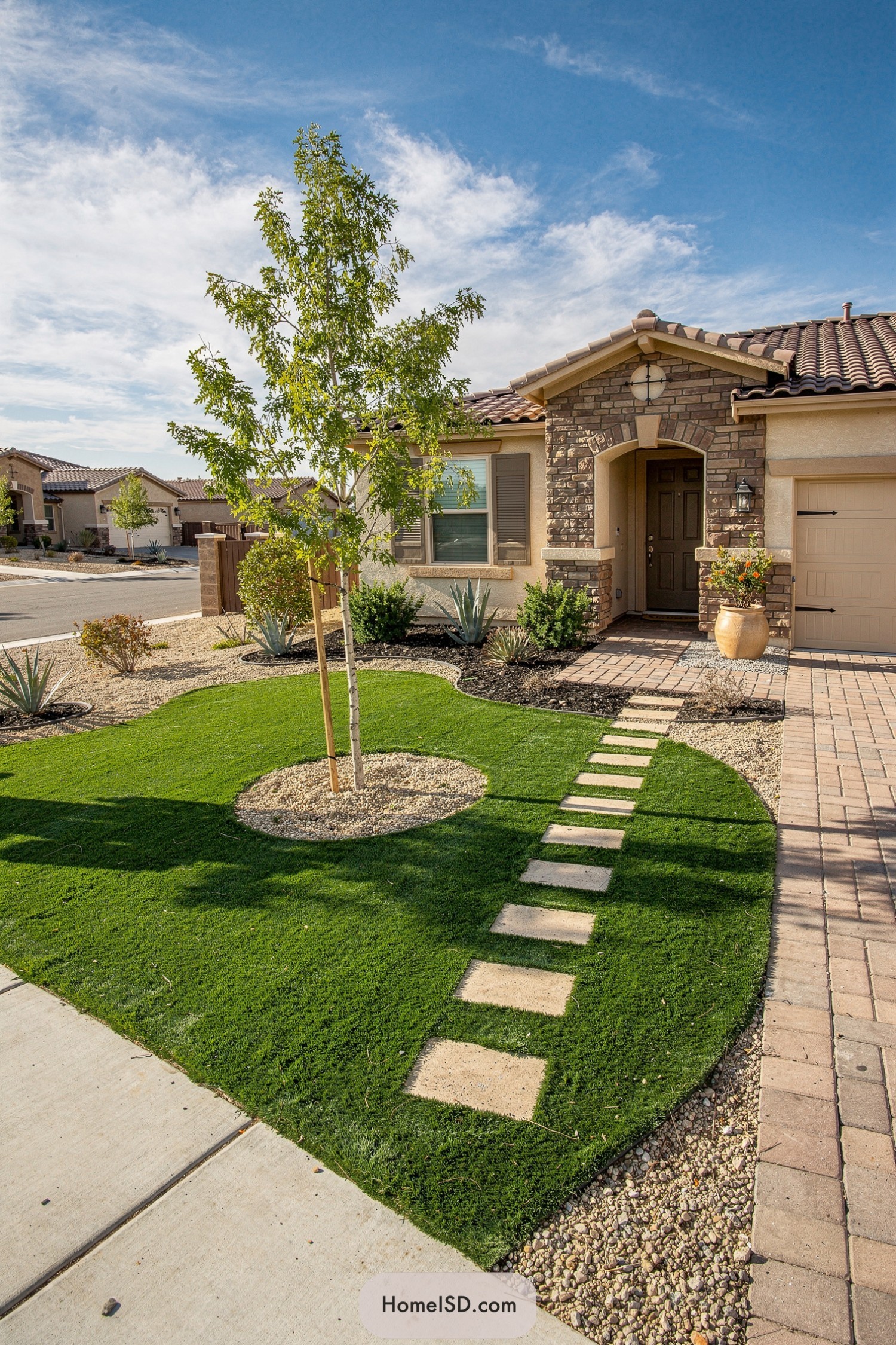 Front yard with bright turf, central tree, and stepping-stone path leading to the entry