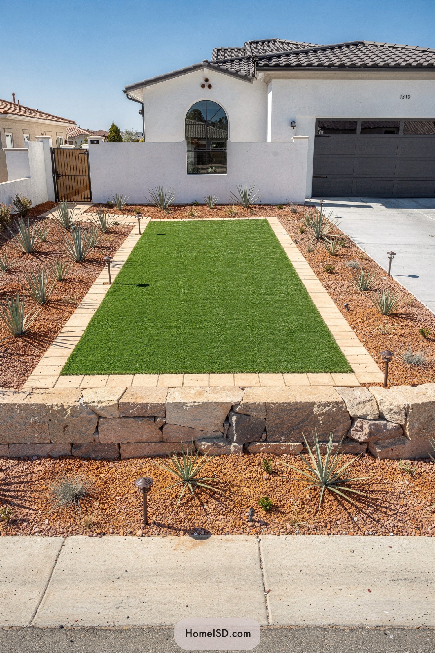 Rectangular artificial lawn framed by stone border and desert plants