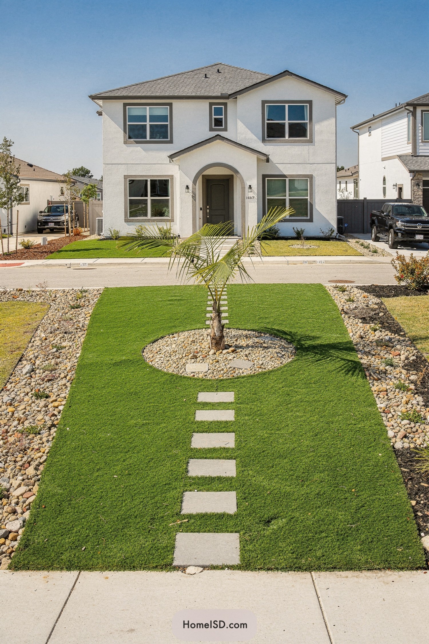 Rectangular turf front yard with stepping stones leading to a central palm tree in a circular rock bed