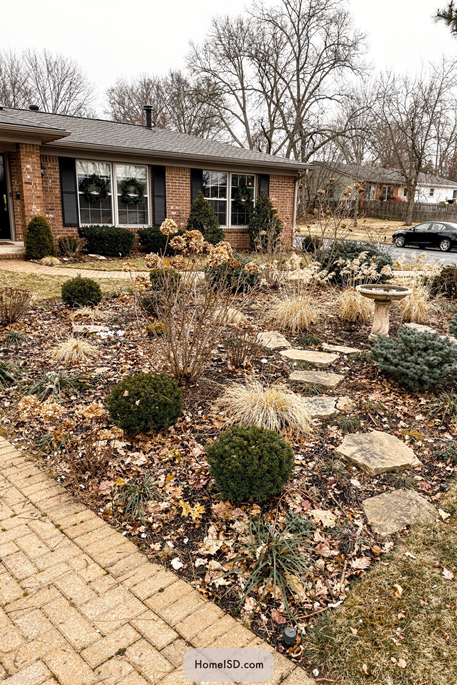 Winter front yard with dried grasses stone path and birdbath in front of a brick house
