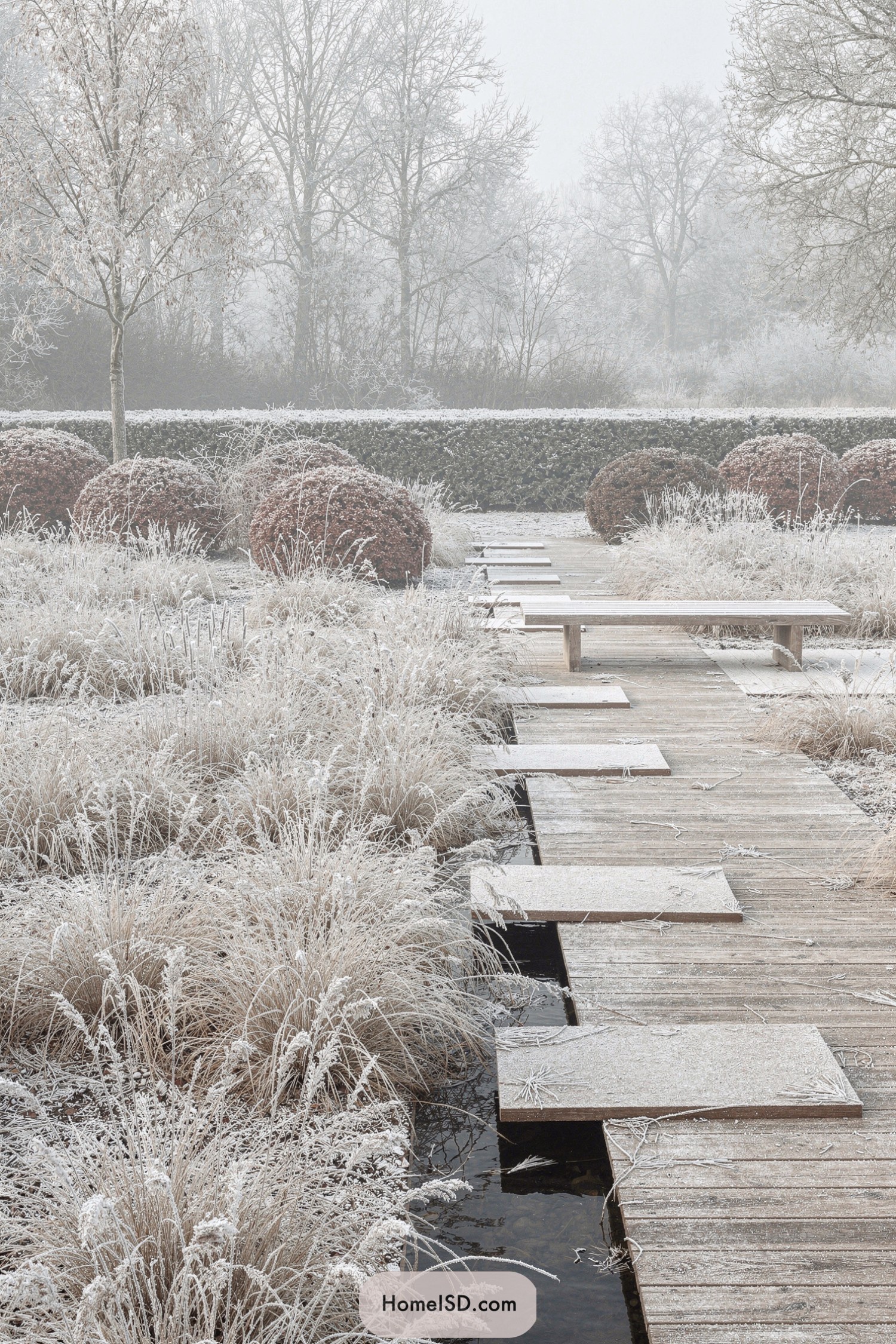 Wooden winter garden boardwalk with frosted grasses, round shrubs, and a simple bench
