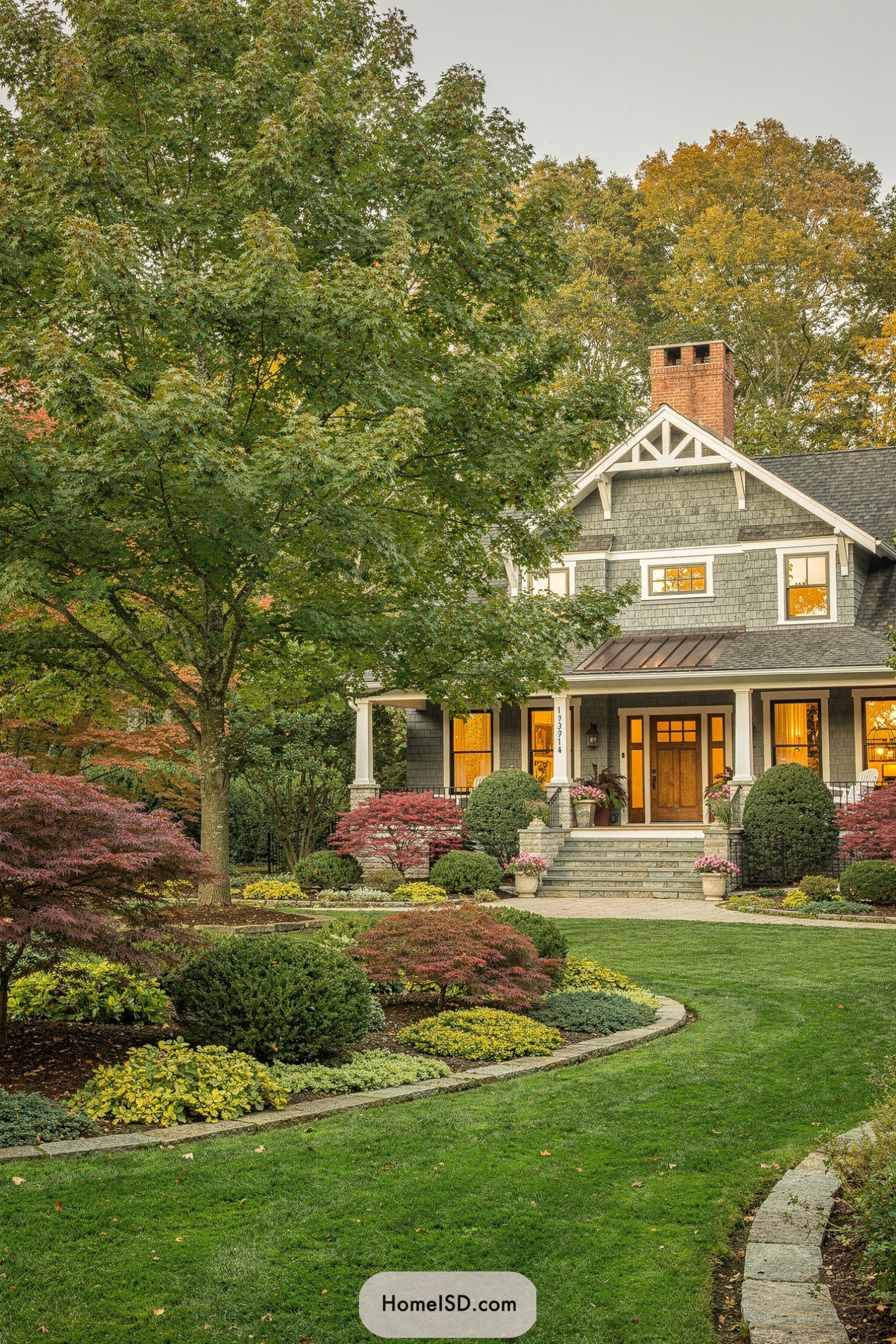 Front yard with large maples, curved lawn, and layered garden beds framing a Craftsman-style home