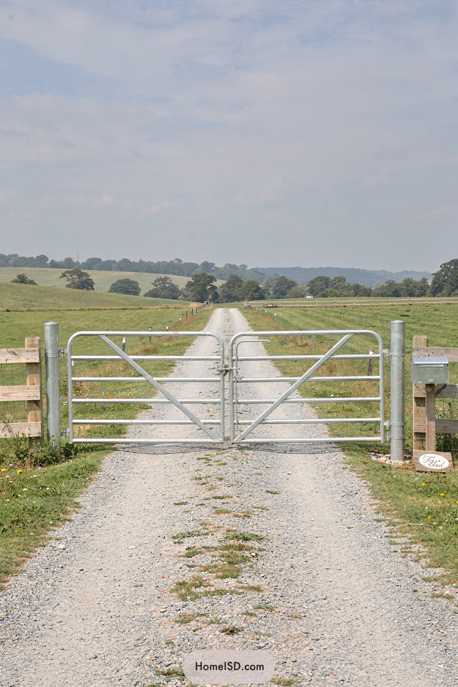 Galvanized metal farm gate across gravel lane