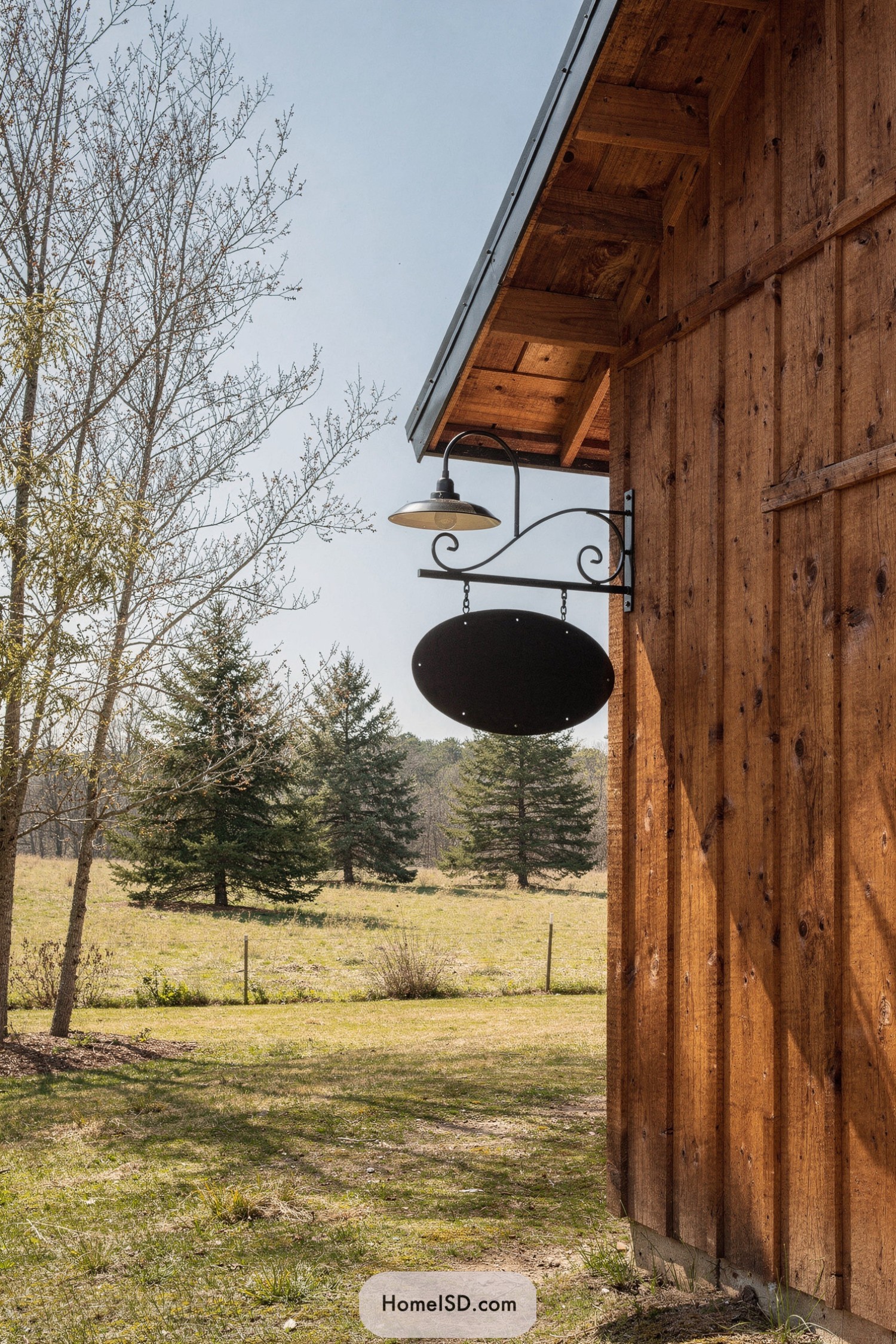 Black hanging oval farm sign on rustic wood barn wall