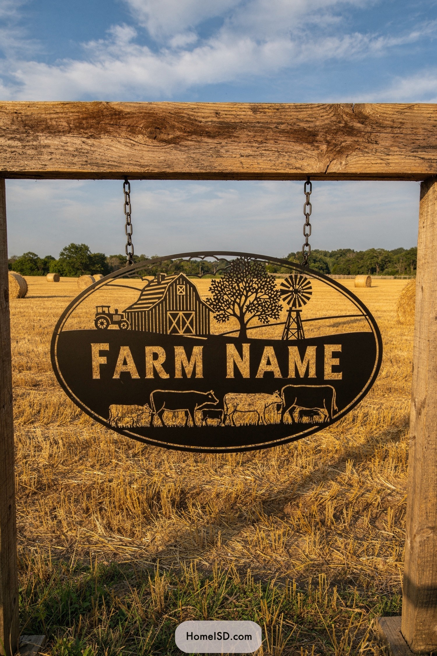 Oval metal farm sign with barn and cows scene hanging from wooden frame in a harvested field