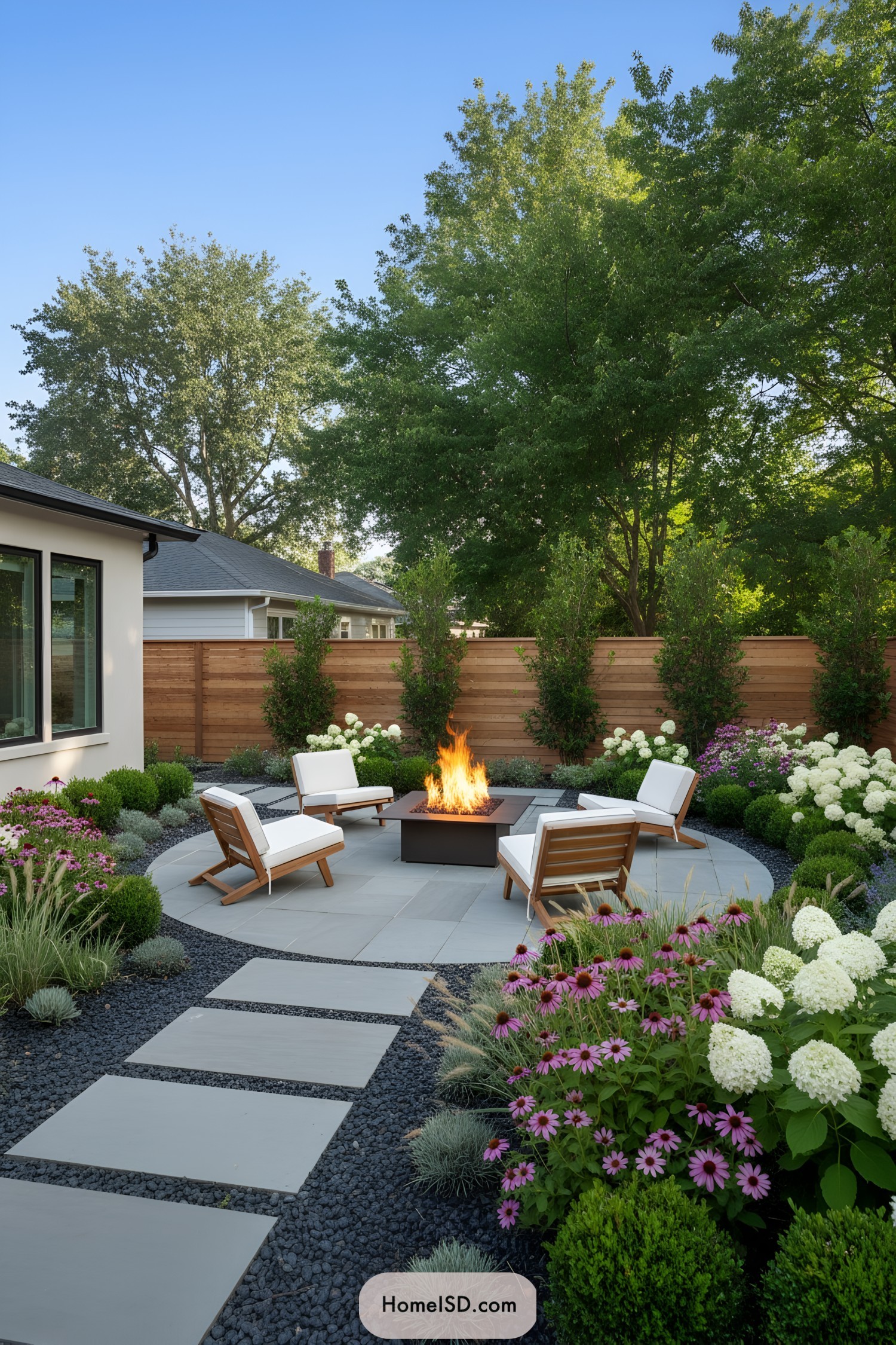 Contemporary backyard fire pit with modern chairs and lush flowering garden beds