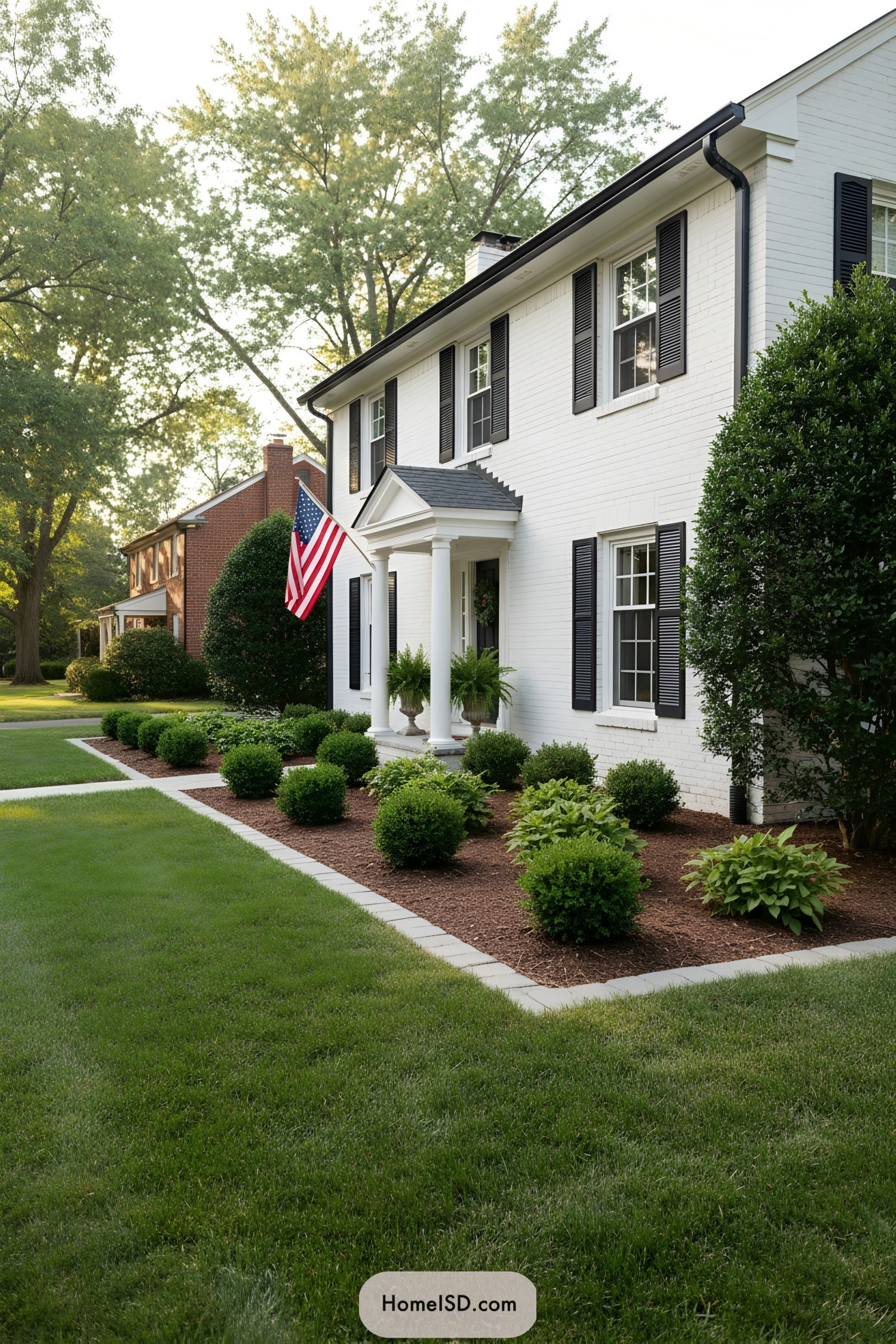 Neatly edged front garden with boxwood shrubs lining a white brick house