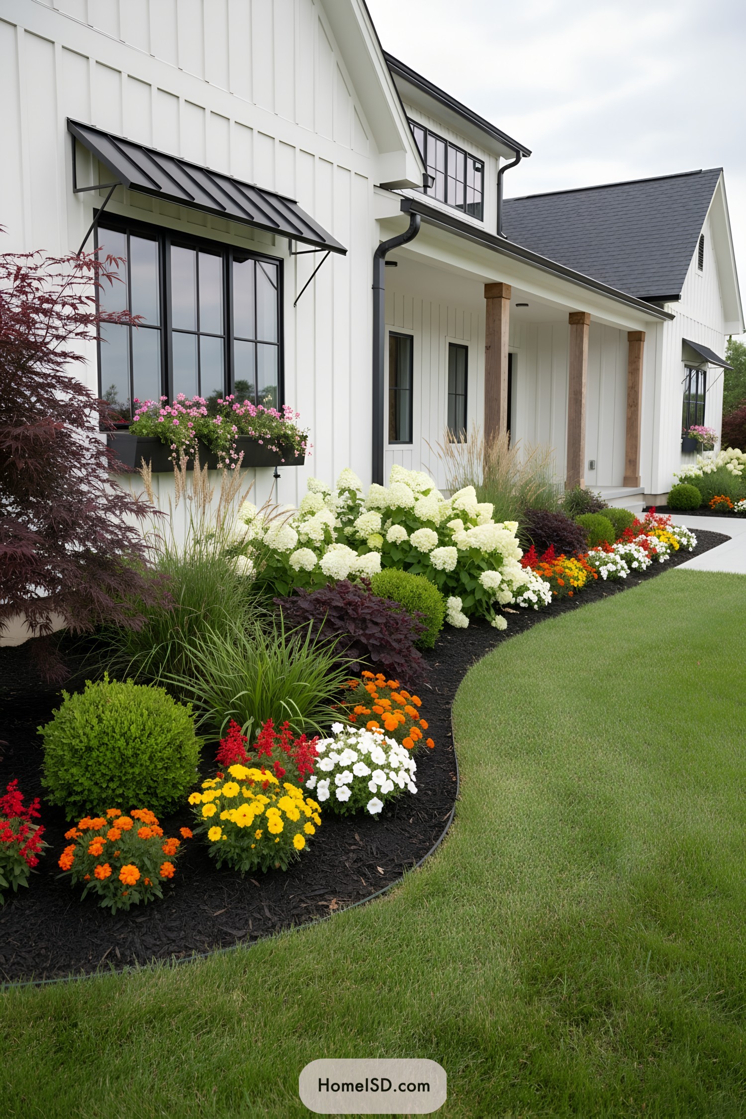 Curved front yard flower bed along white farmhouse with colorful annuals and hydrangeas