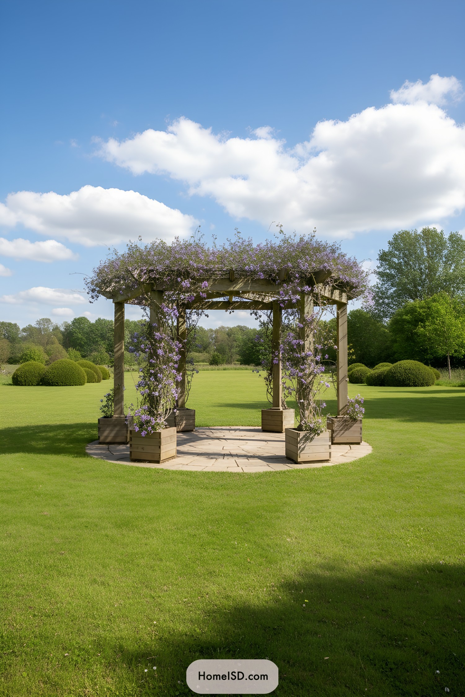 Wooden pergola wrapped in purple flowering vines on a circular stone pad in the middle of a large manicured lawn