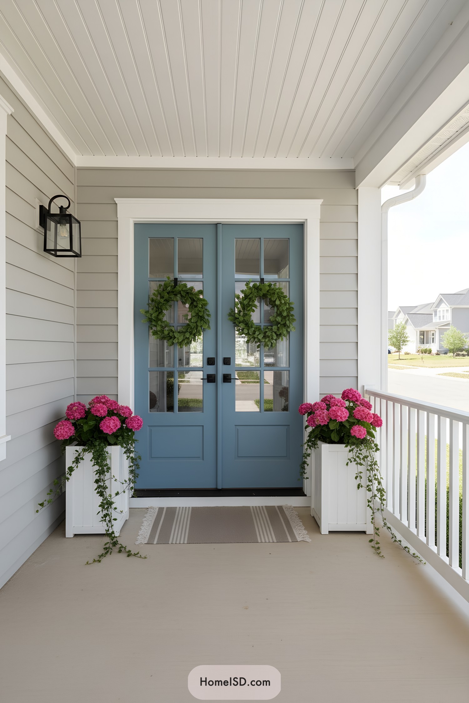 Blue double front doors with leafy wreaths and white planters of pink hydrangeas on a clean, modern porch