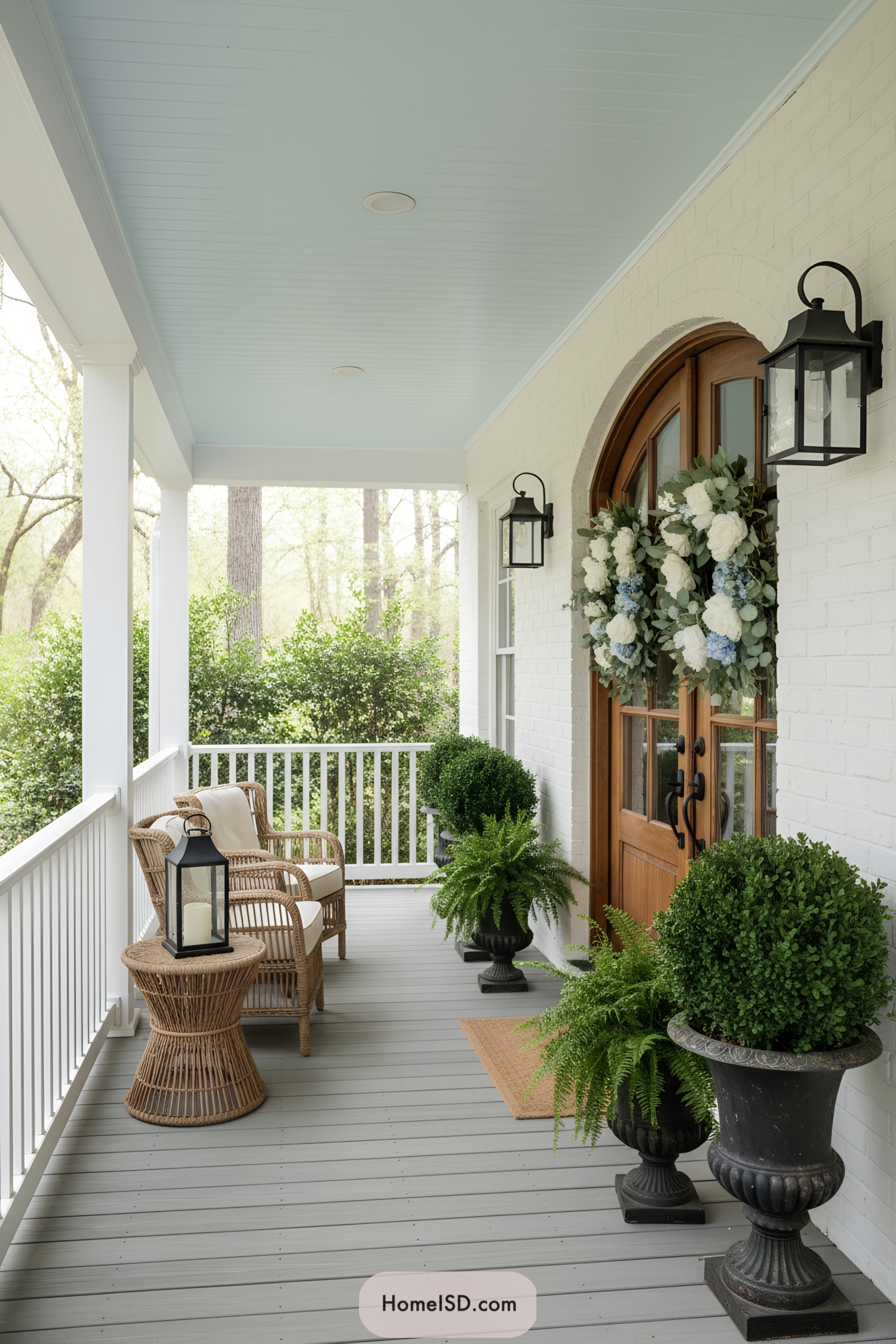 Spring porch with wicker seating, urn planters, and double floral wreaths on a wooden door