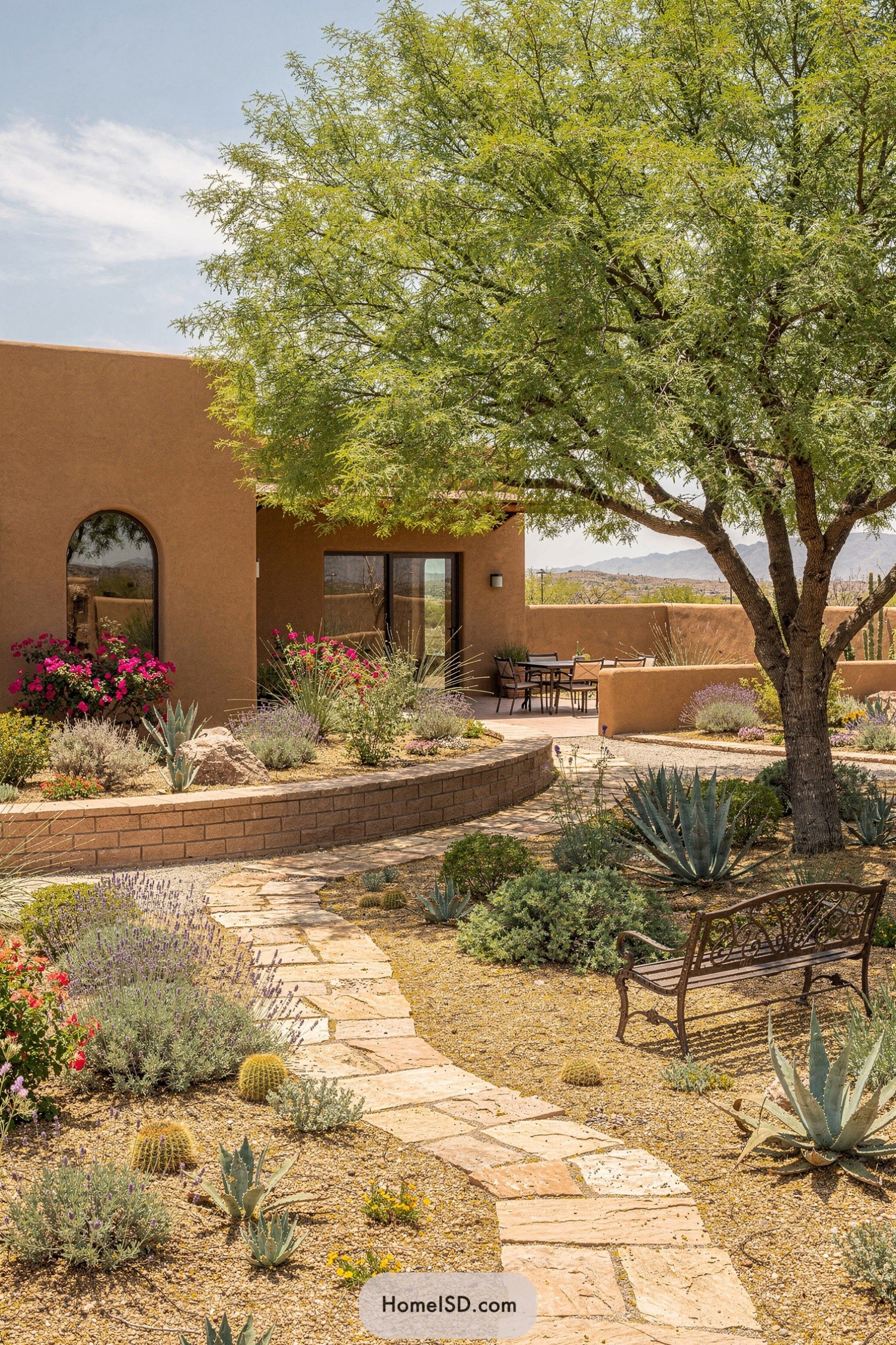Southwestern adobe home with xeriscape garden, curved stone path, and shaded seating under a large tree