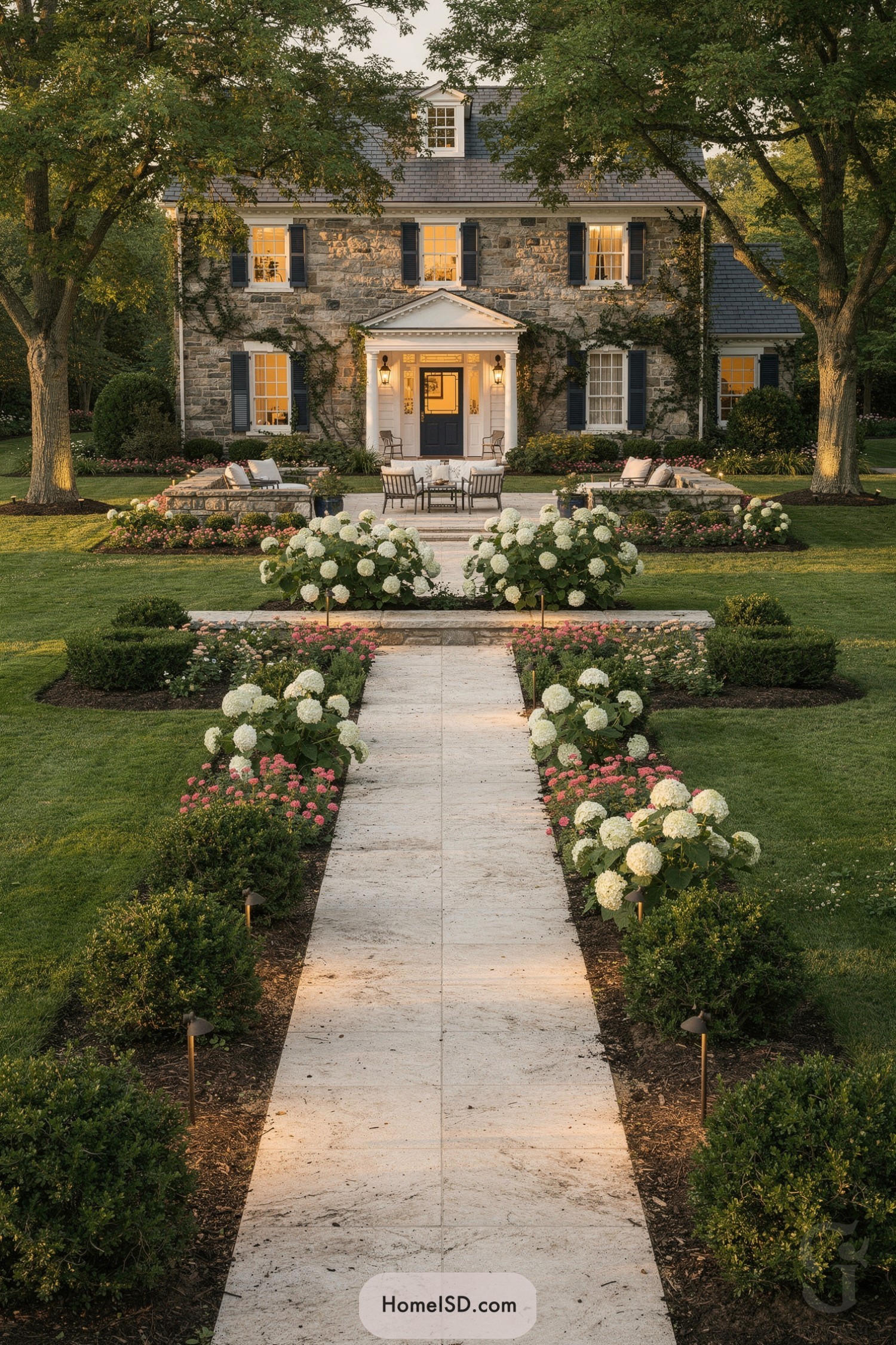 Stone walkway lined with hydrangeas leading to a classic stone house